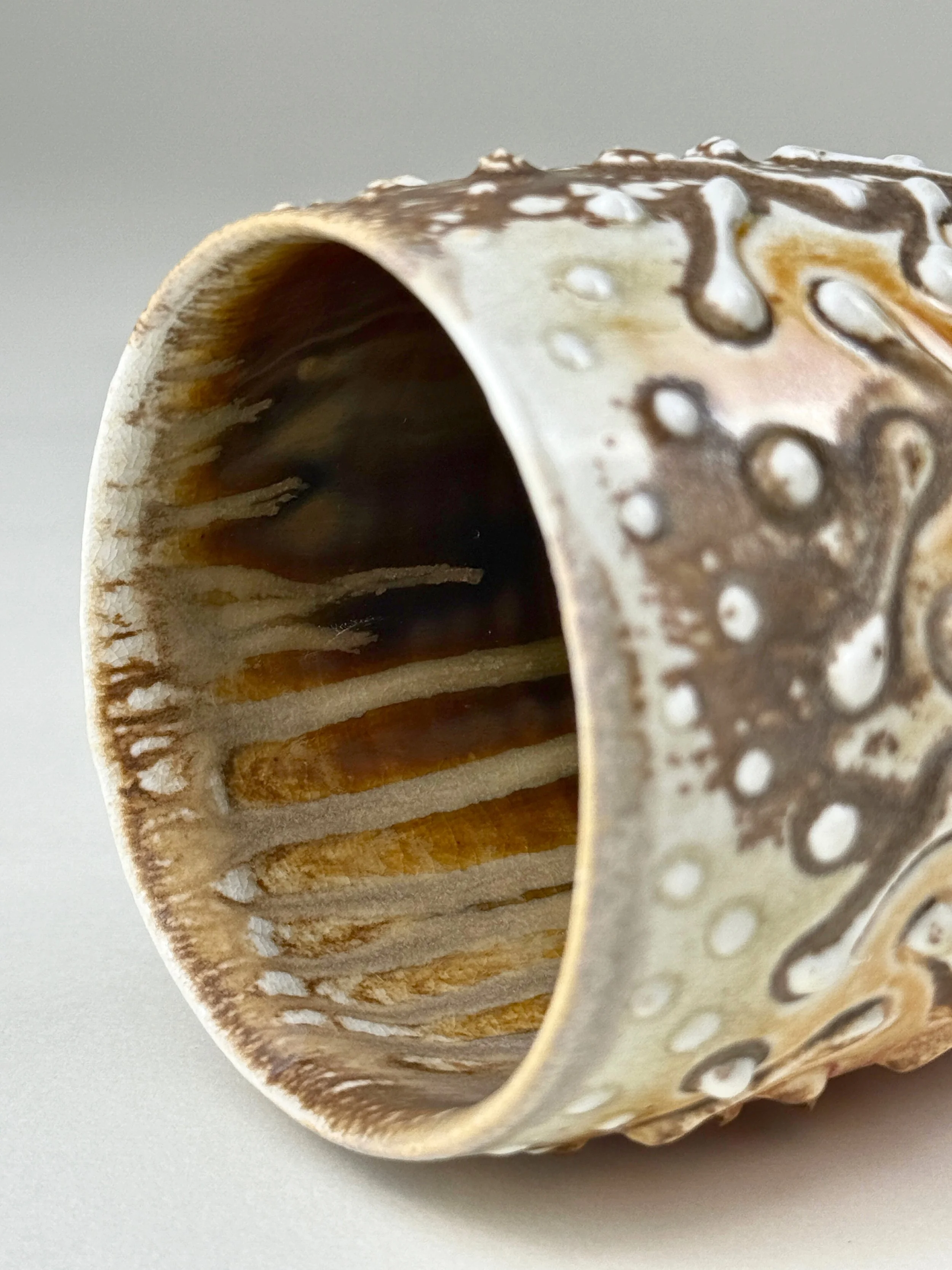 Close-up of a ceramic cup with a textured, patterned exterior and interior, showcasing earthy tones and decorative dots.