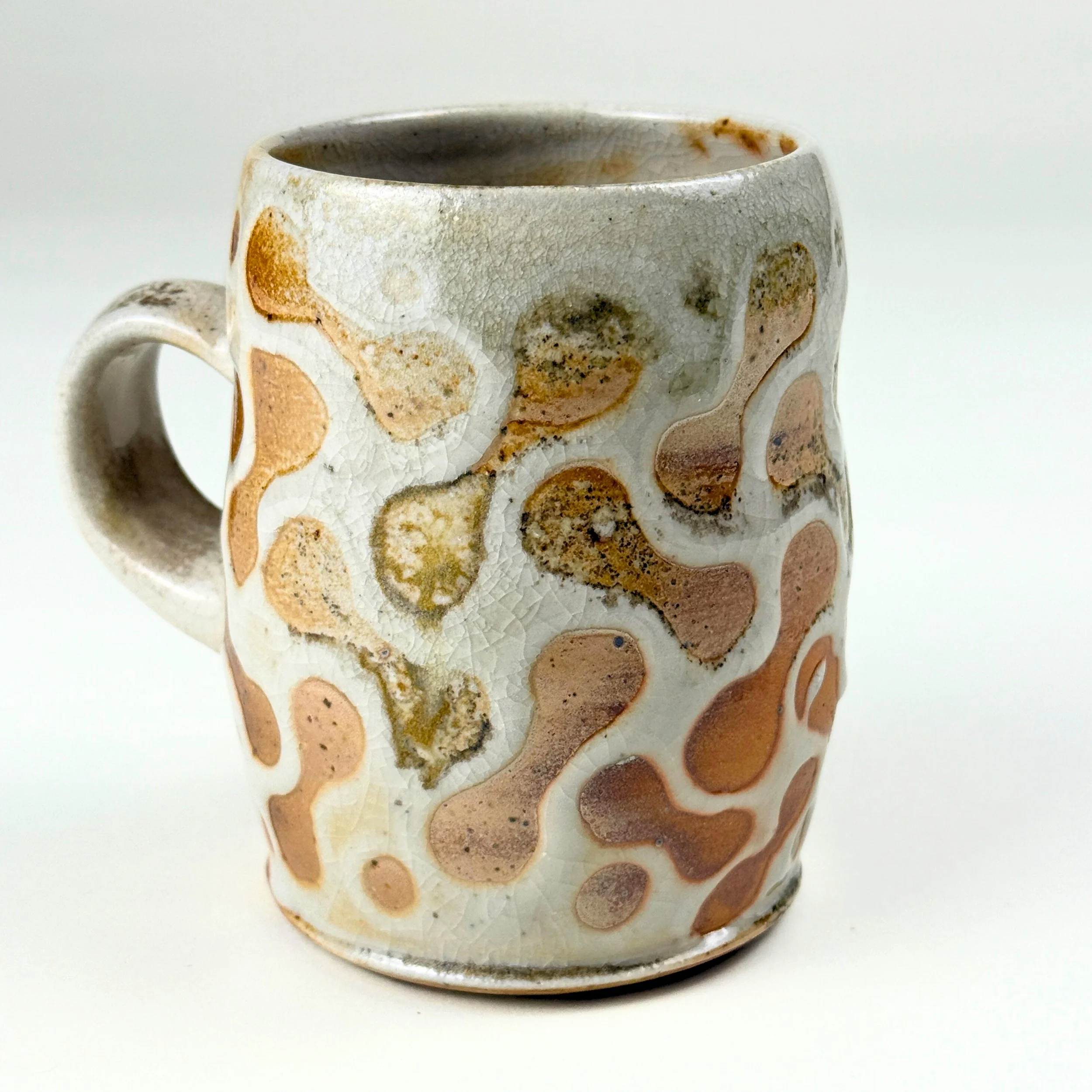 A ceramic mug with a crackled glaze finish and abstract brown, beige, and white splotches.