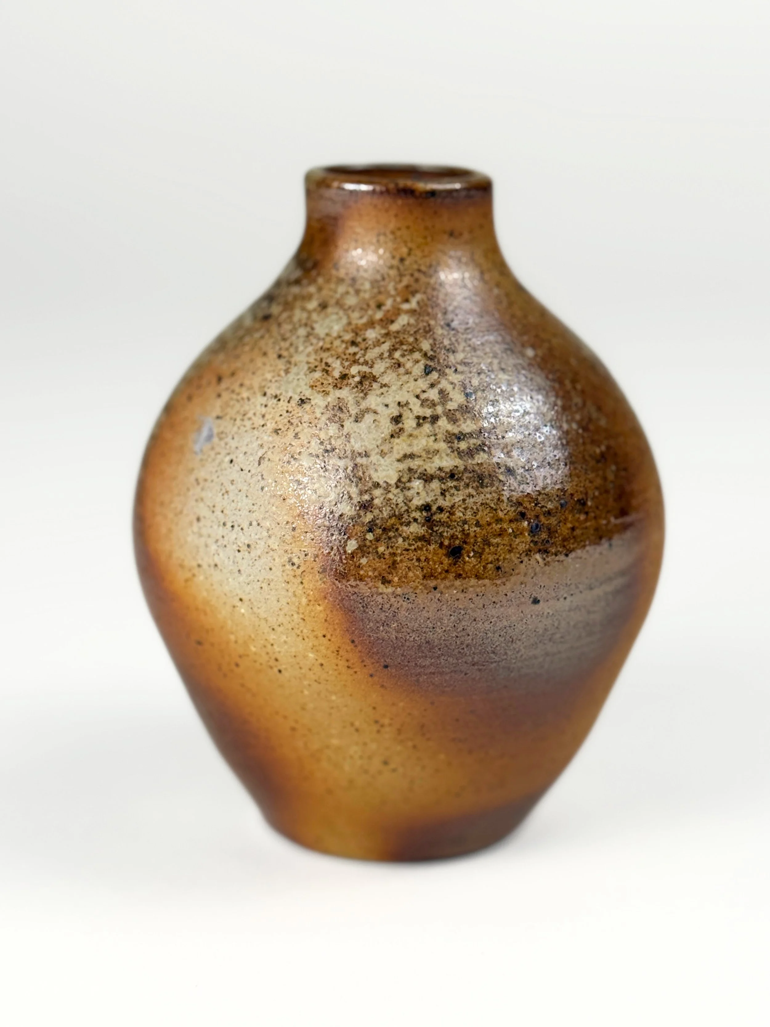 Ceramic vase with a textured, earthy glaze in brown, beige, and tan tones, on a plain white background.