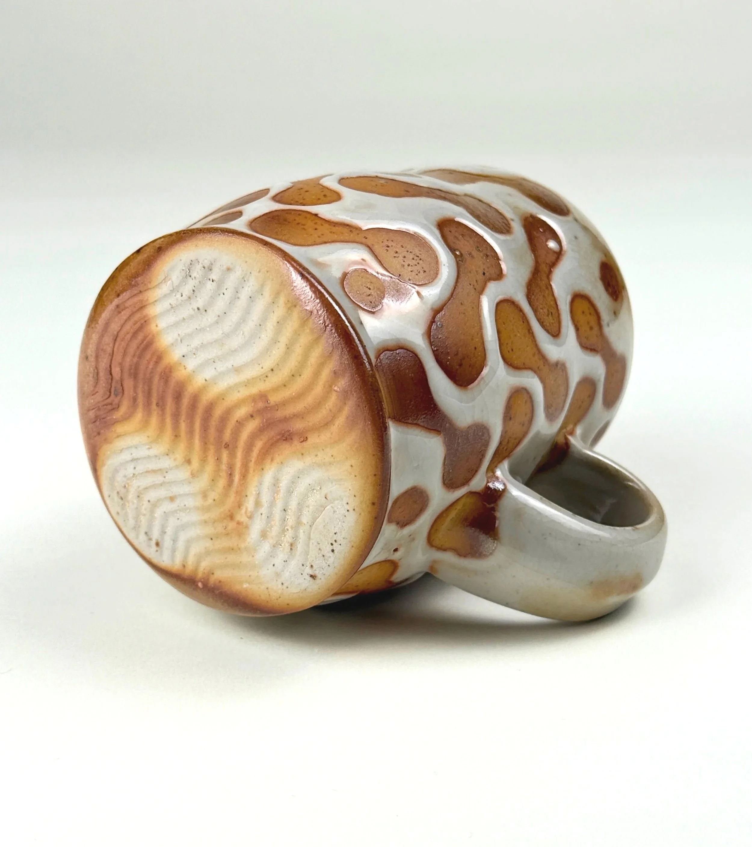Ceramic mug with giraffe pattern, lying on its side, with the open mouth facing to the right, on a white surface.