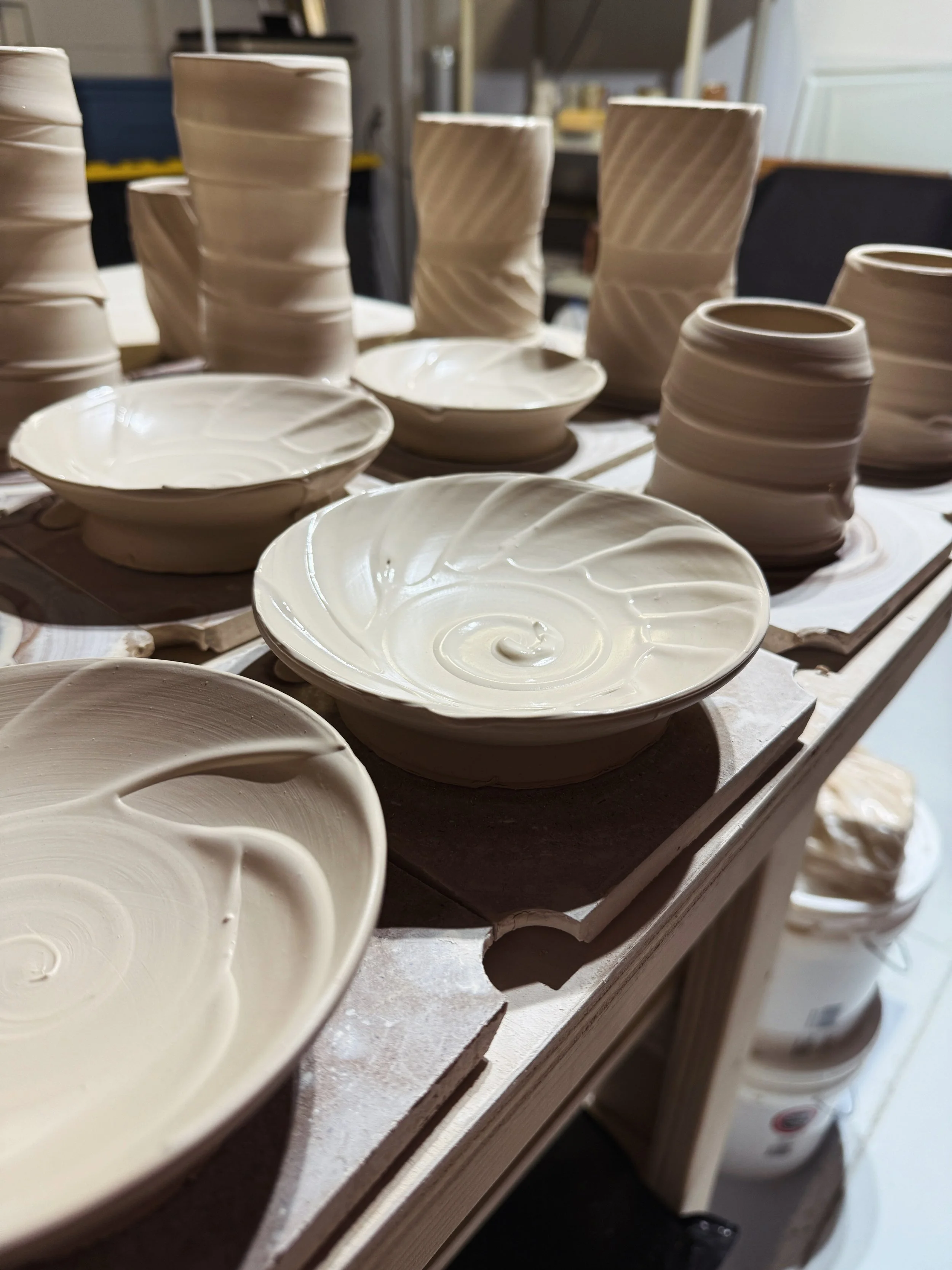 Unfinished ceramic bowls and plates on a work table in a pottery studio.