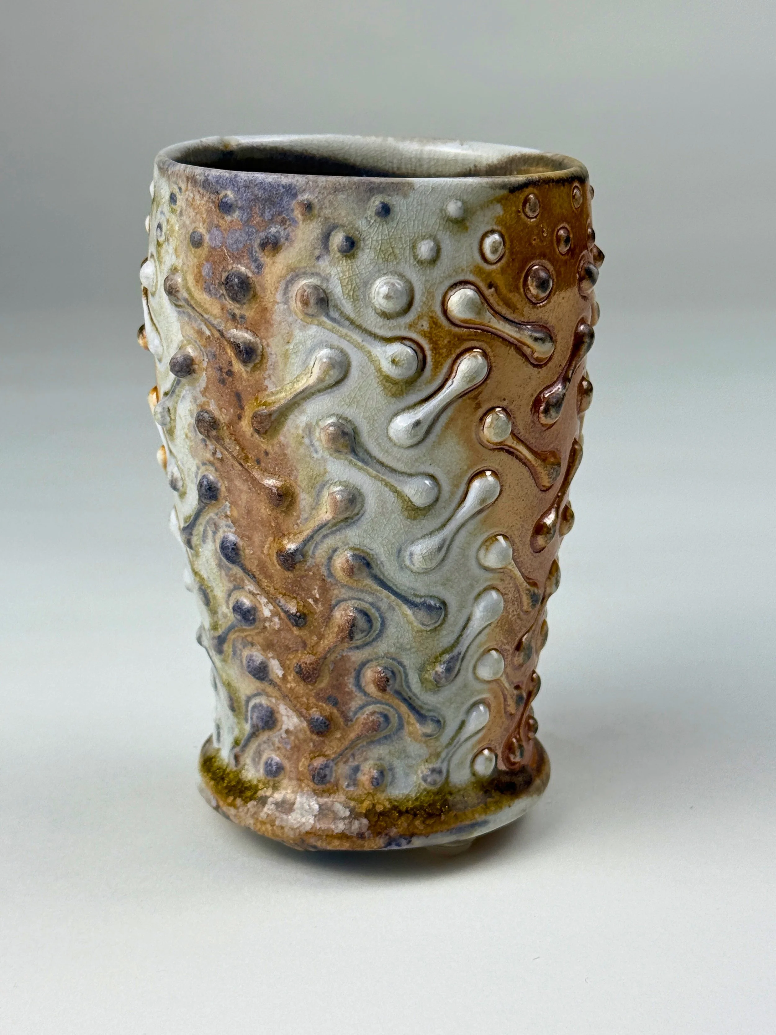 A ceramic mug with textured, raised patterns and a multicolored glaze, primarily in earthy tones like brown, beige, and white.