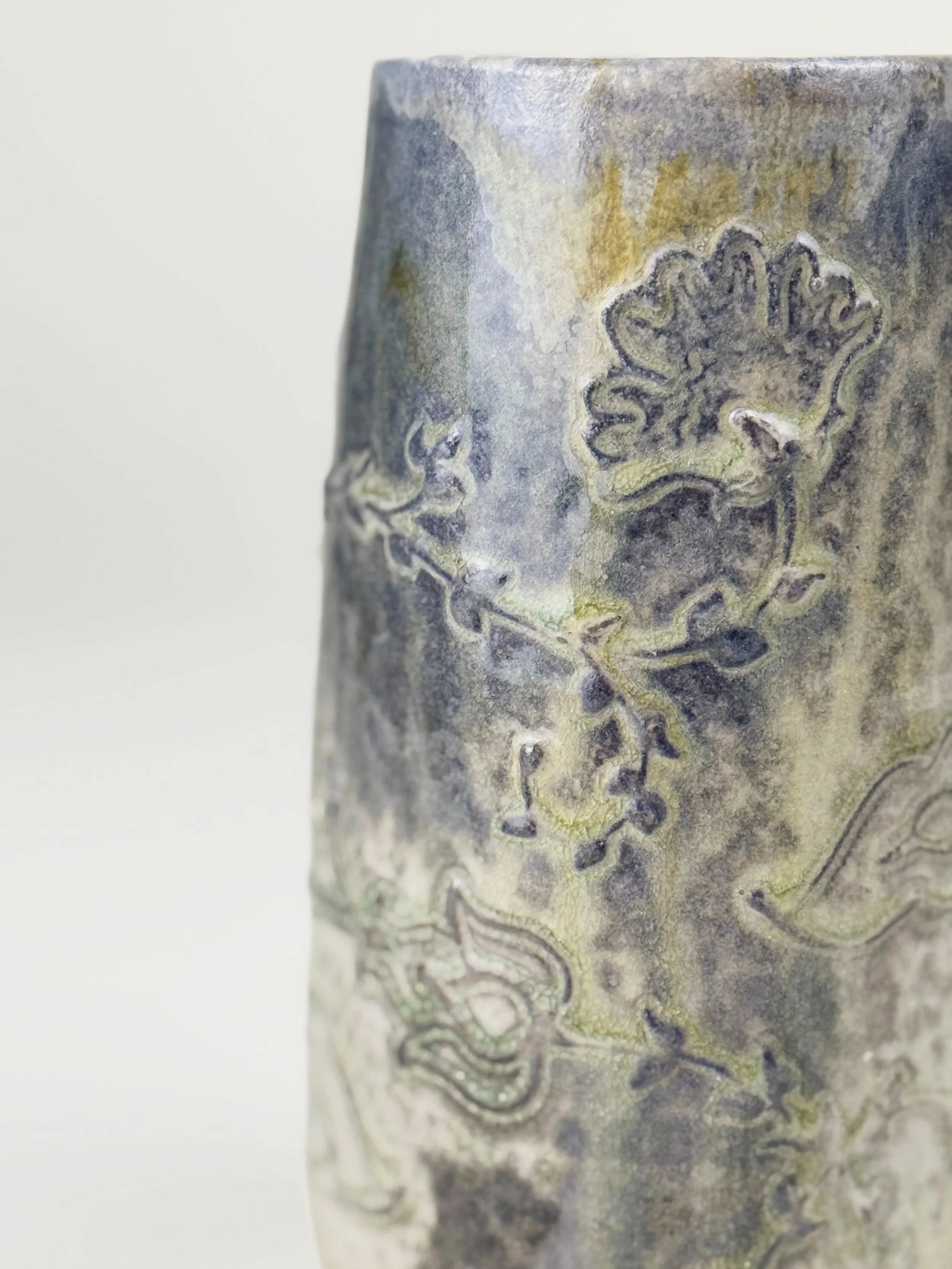 Close-up of a ceramic vase with raised floral and vine designs in a weathered gray glaze.