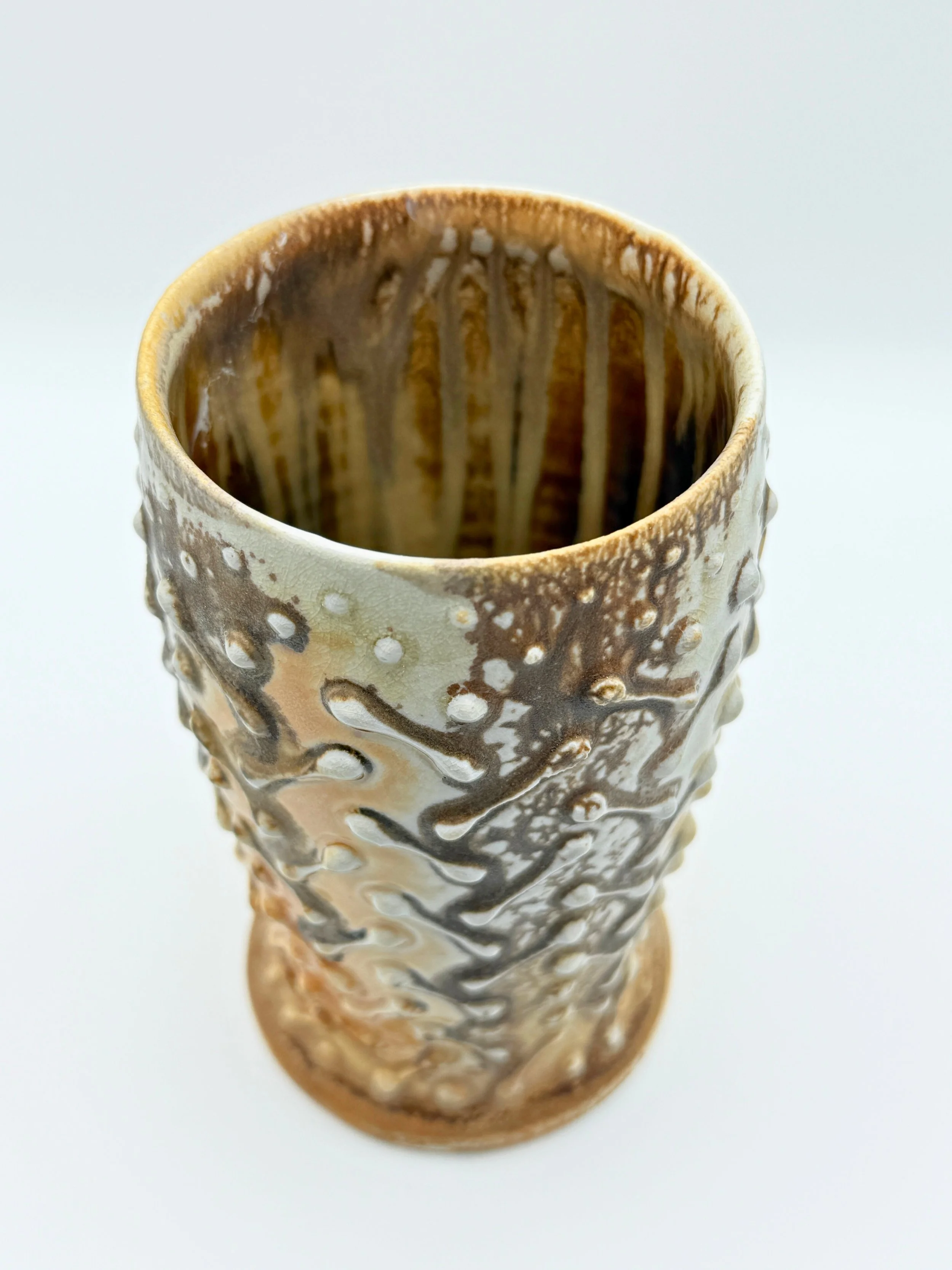 A close-up of a tall ceramic mug with a speckled, textured surface and brown and beige glaze, viewed from above.