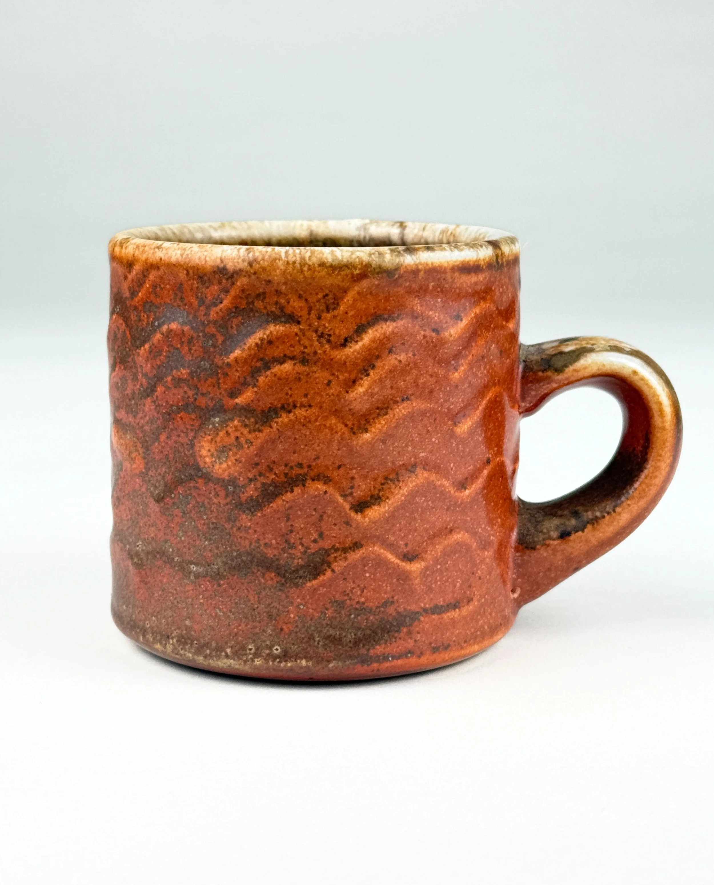 A ceramic mug with textured wavy patterns in reddish-brown tones against a plain white background.