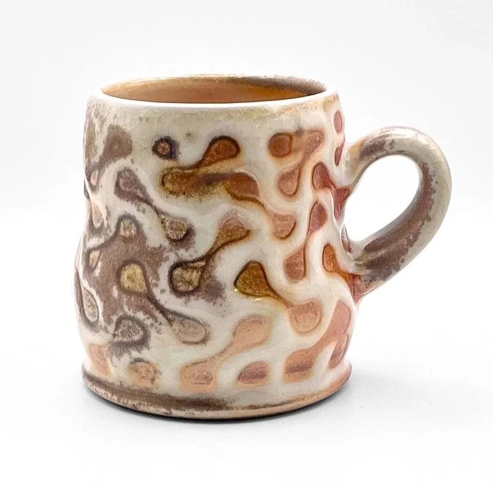 Decorative ceramic mug with an abstract swirl pattern in earth tones on a white background.