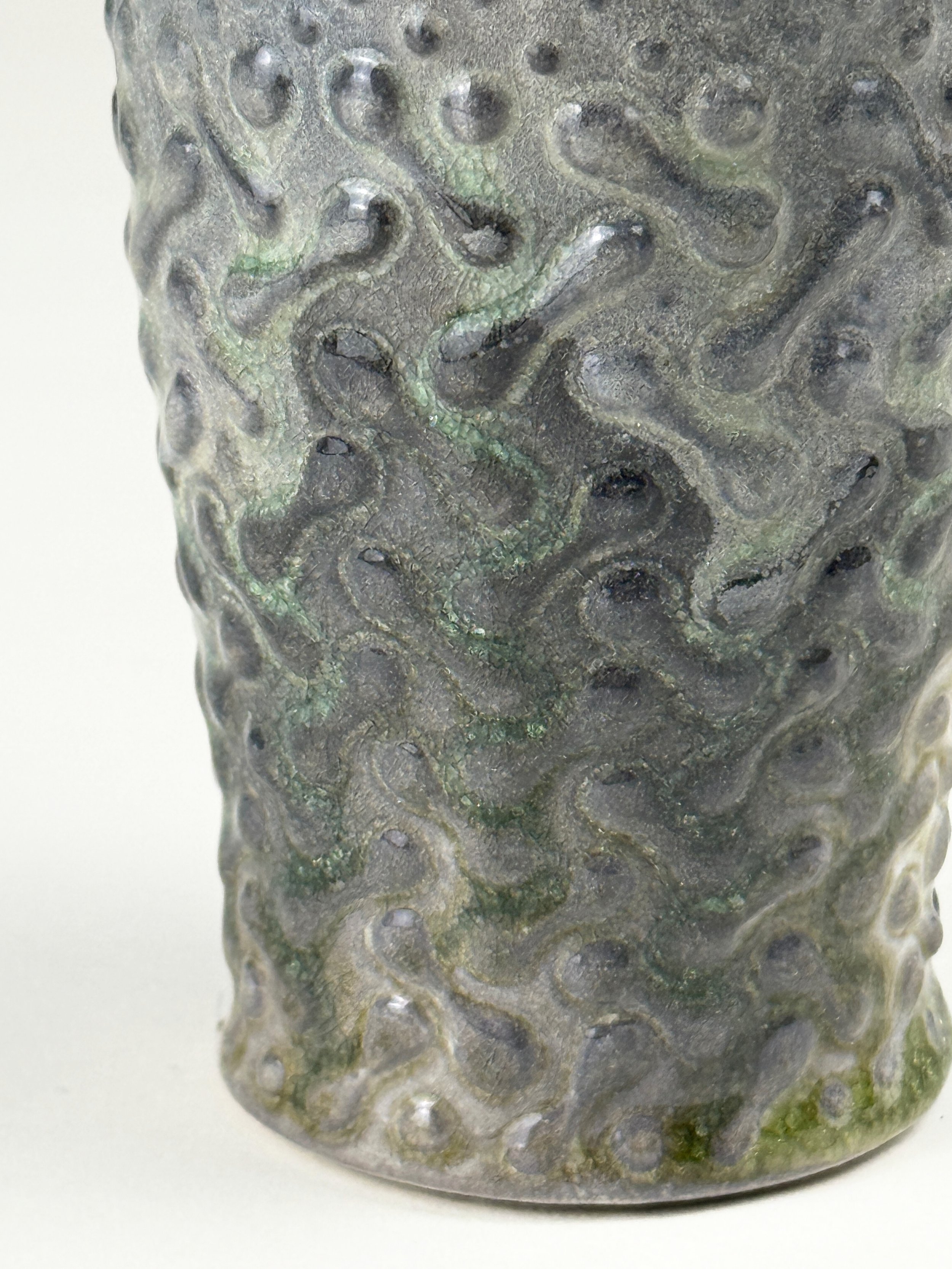 Close-up of a textured, dark-colored ceramic or metal container with swirling, irregular patterns.