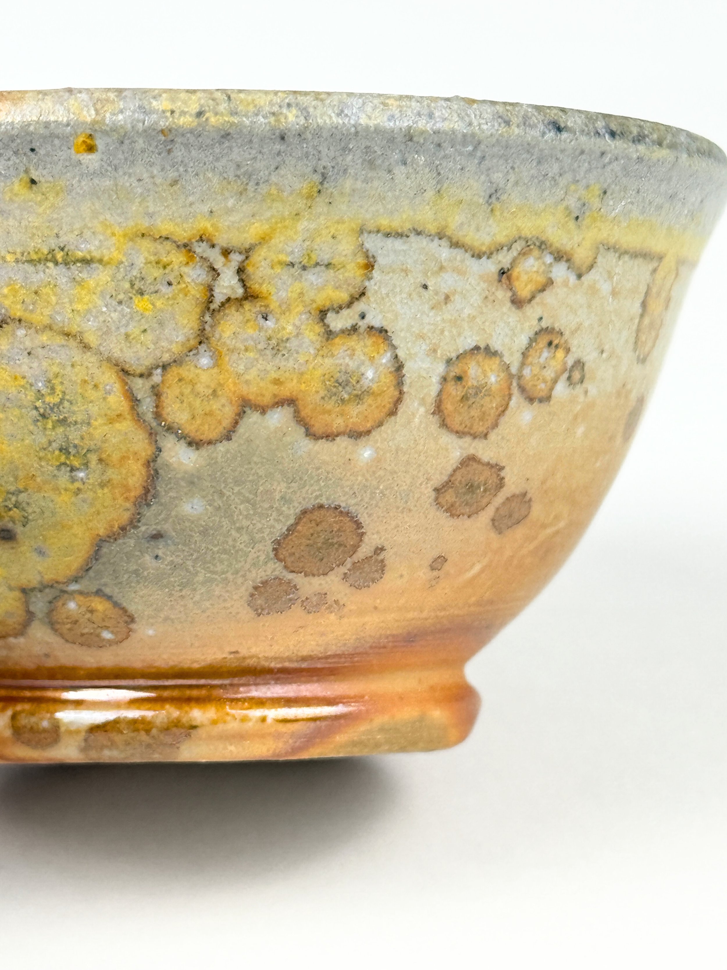 Close-up photo of the side of a ceramic bowl with an earthy tone and a speckled glaze pattern.