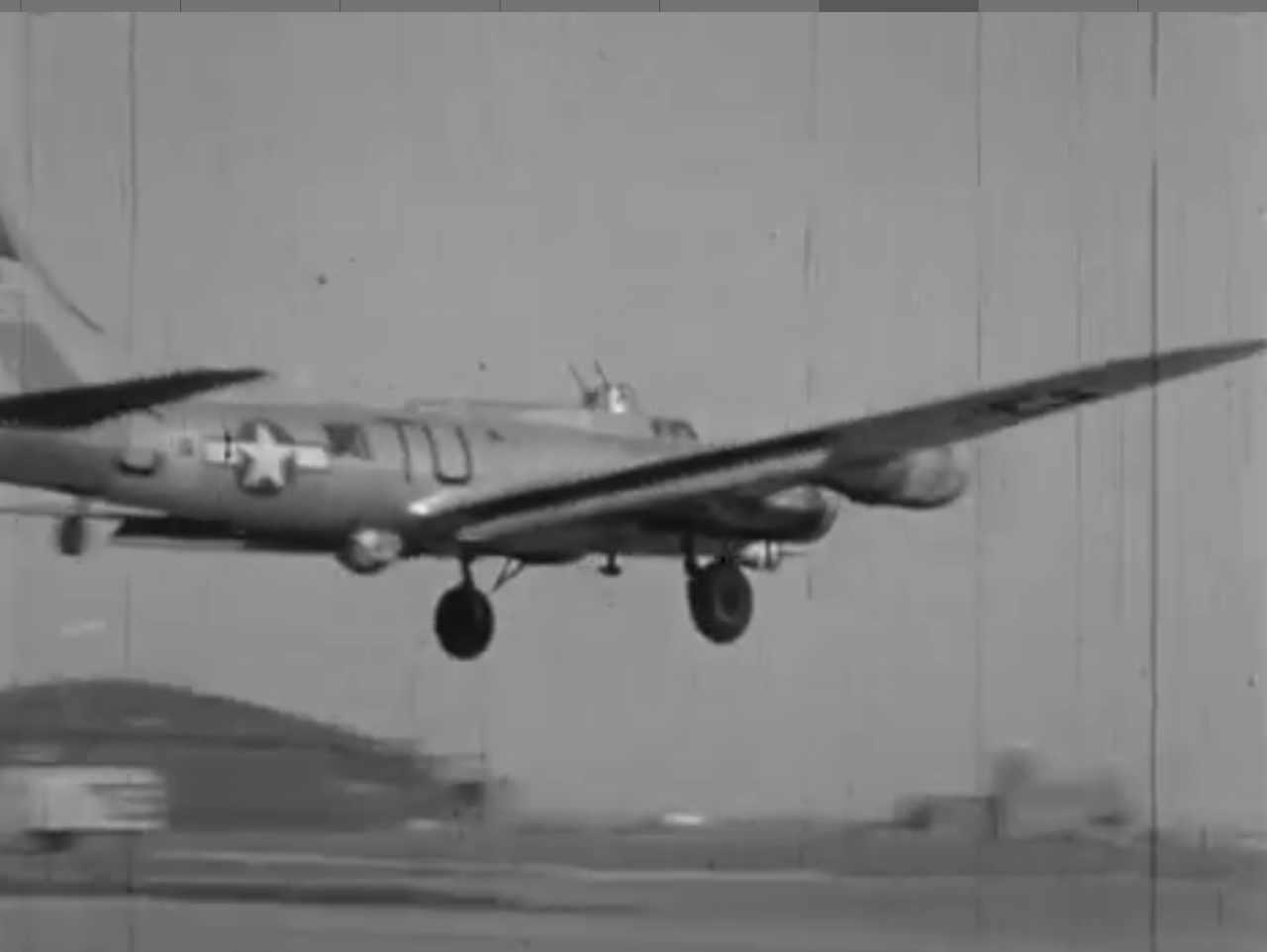 A vintage black-and-white photograph of a military aircraft with a star insignia on the fuselage, in mid-flight, approaching a runway or landing area.
