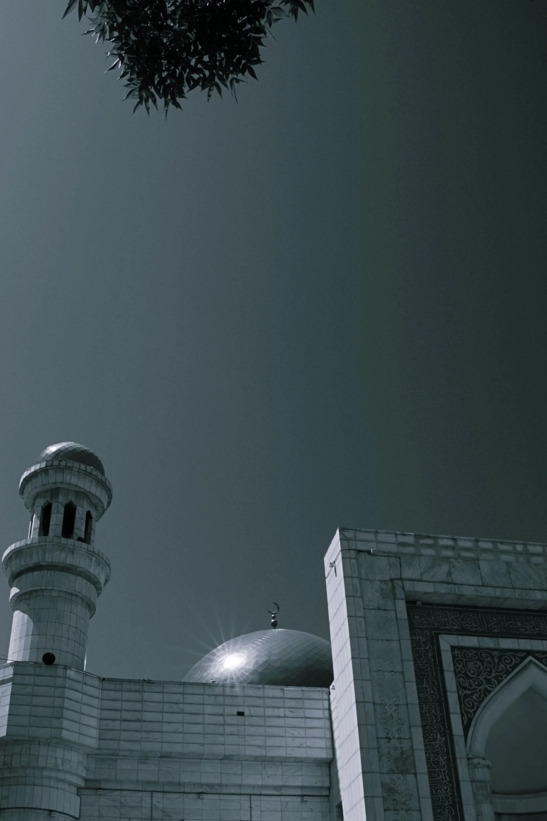 A photograph of a mosque with a large dome, two minarets, intricate window designs, and detailed exterior decorations, taken from a low angle during daylight.