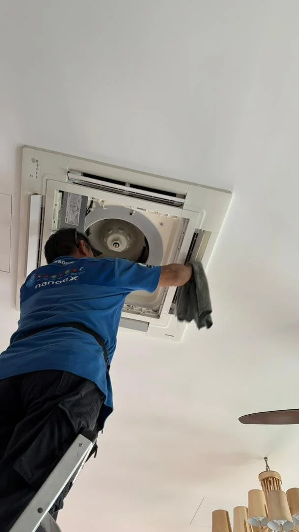 Technician cleaning an air conditioning unit mounted on the ceiling.