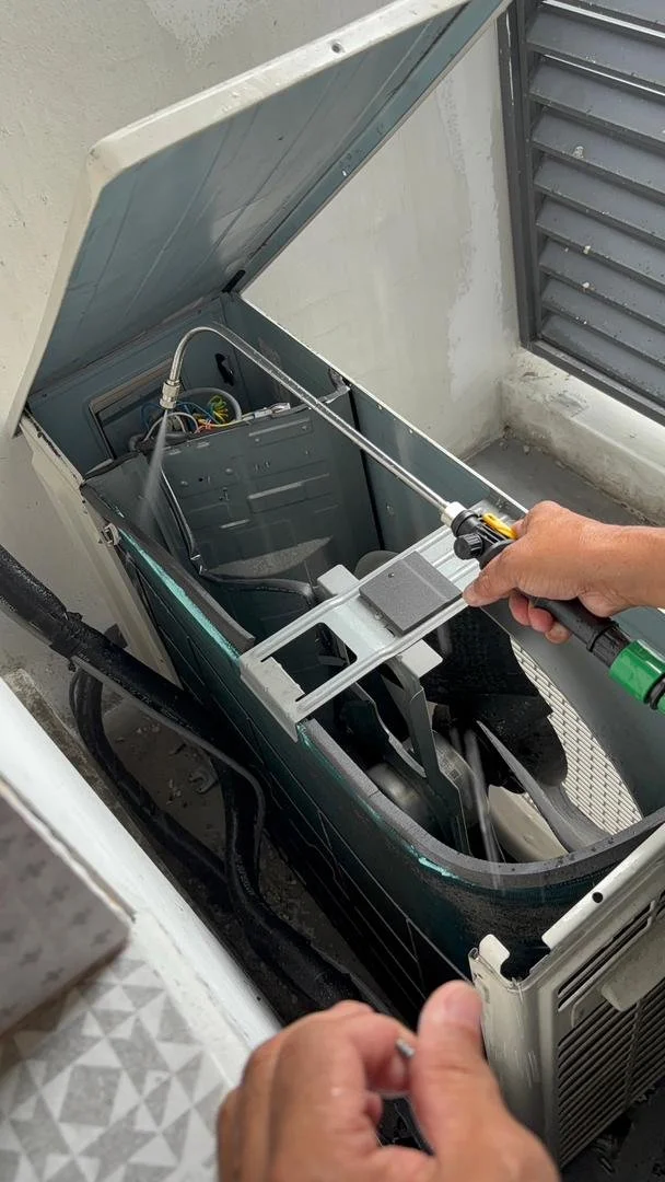 Person servicing an outdoor air conditioning unit with a spray gun.