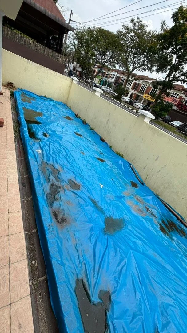 Construction and renovation service . A blue tarp laid out on a sidewalk against a yellow wall, with wet patches and dark spots, possibly water or dirt, scattered across its surface.