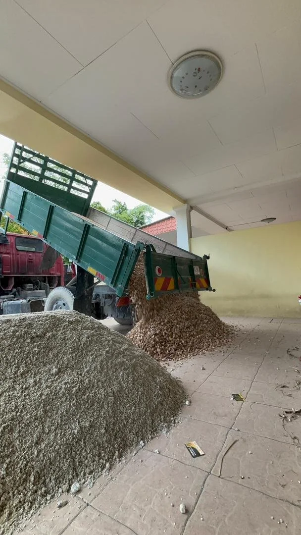 A truck unloading a large pile of gravel or small stones inside a covered area with a yellow wall and a ceiling light fixture.