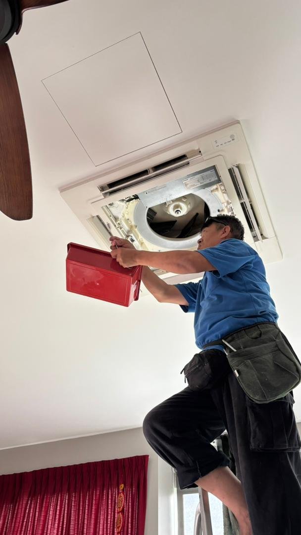 Technician installing or repairing a ceiling-mounted air conditioning unit with a red toolbox.
