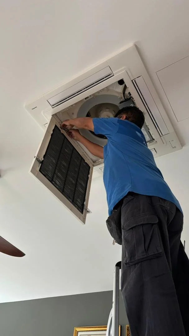 A technician installing or repairing a ceiling-mounted air conditioning unit.