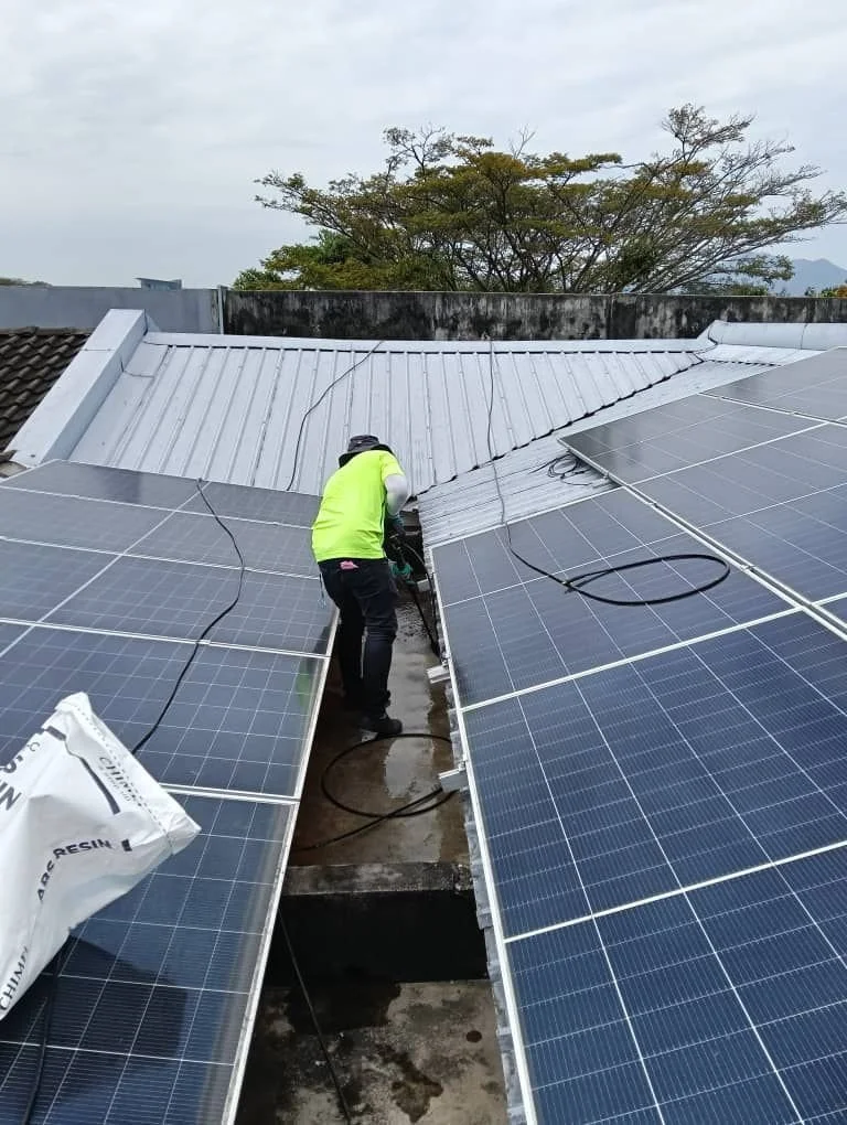 Person installing or maintaining solar panels on a rooftop with trees in the background.