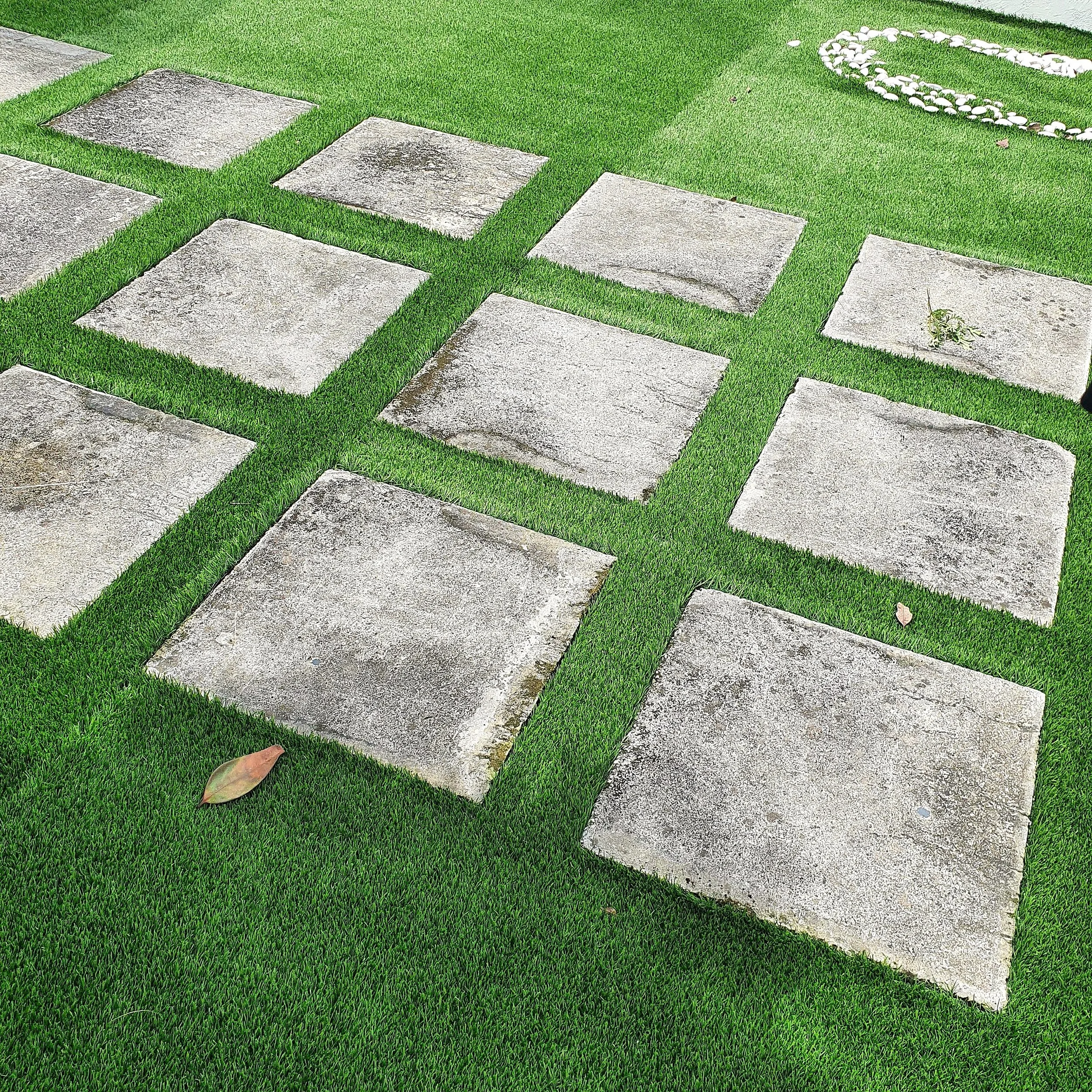 Concrete square stepping stones laid on lush green grass in a pattern.