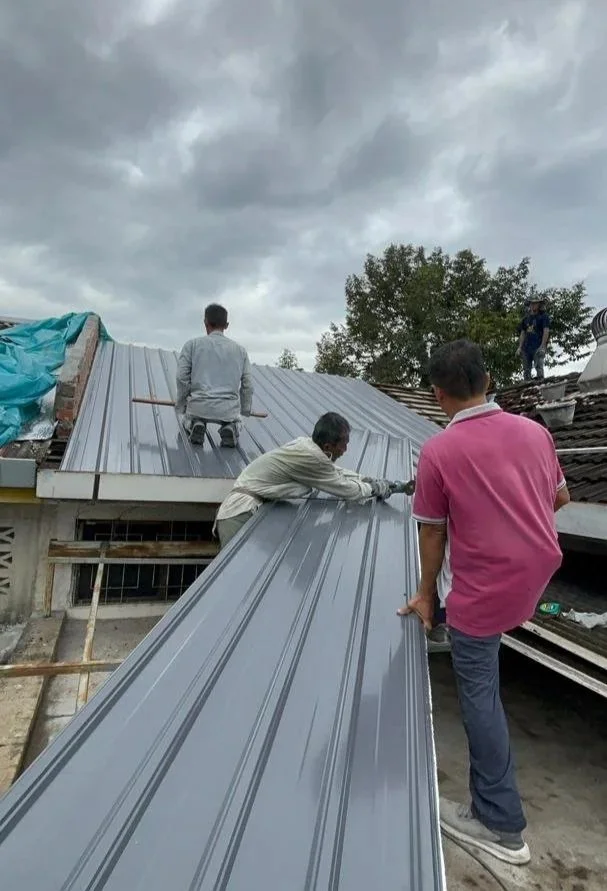 Construction workers installing a metal roof on a building under a cloudy sky.