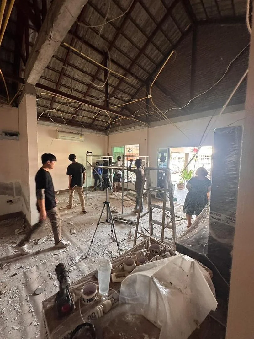 People working inside a building under construction or renovation, with scaffolding, ladders, and construction materials visible.