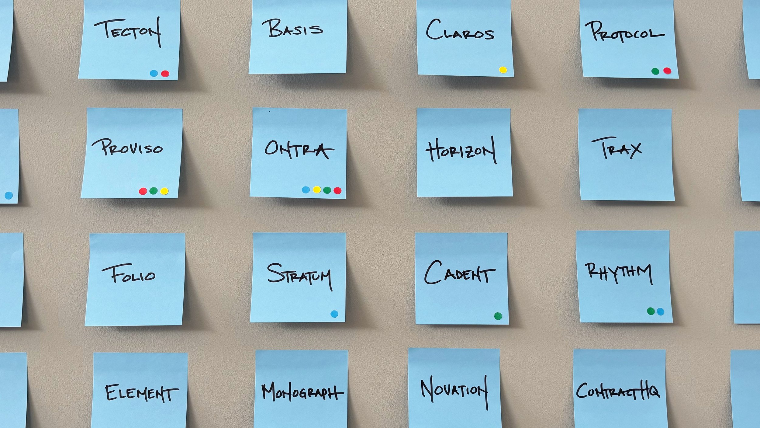 Blue sticky notes with name ideas written in black Sharpie on a gray background. Some sticky notes also have small, circular, colored stickers on them.