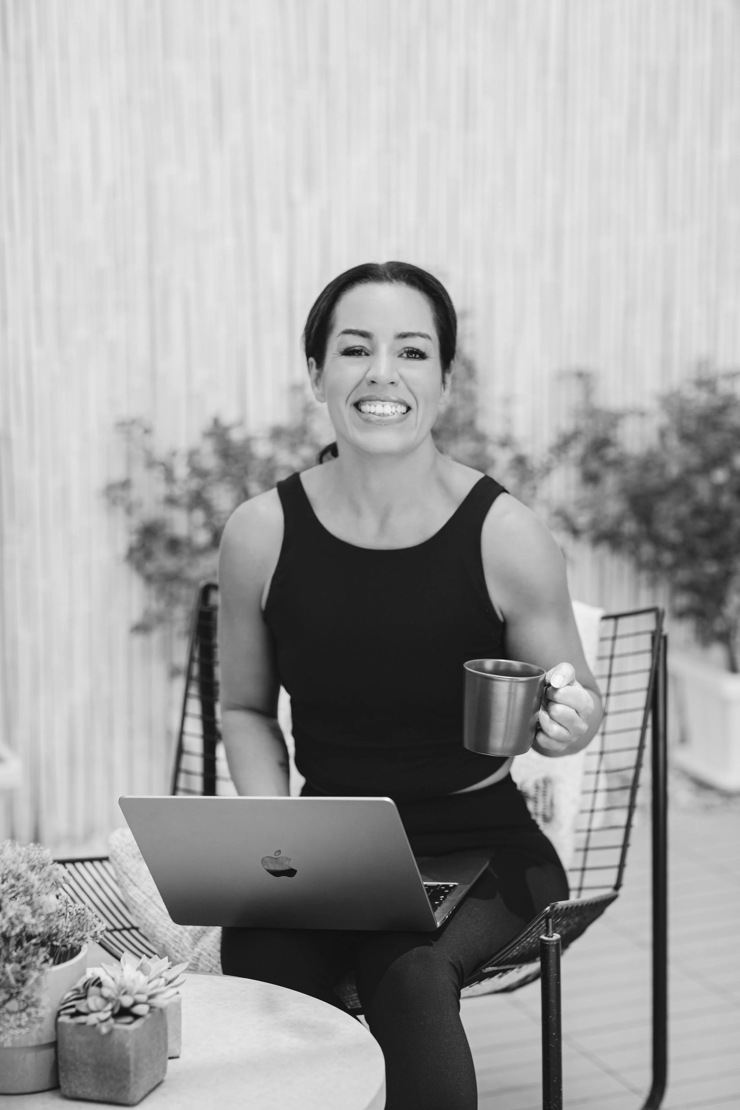 Hayley McClaren is pictured as the health and wellness coach of Inner Architect Coaching. She's wearing a black vest top, holding a cup, looking at the camera and smiling