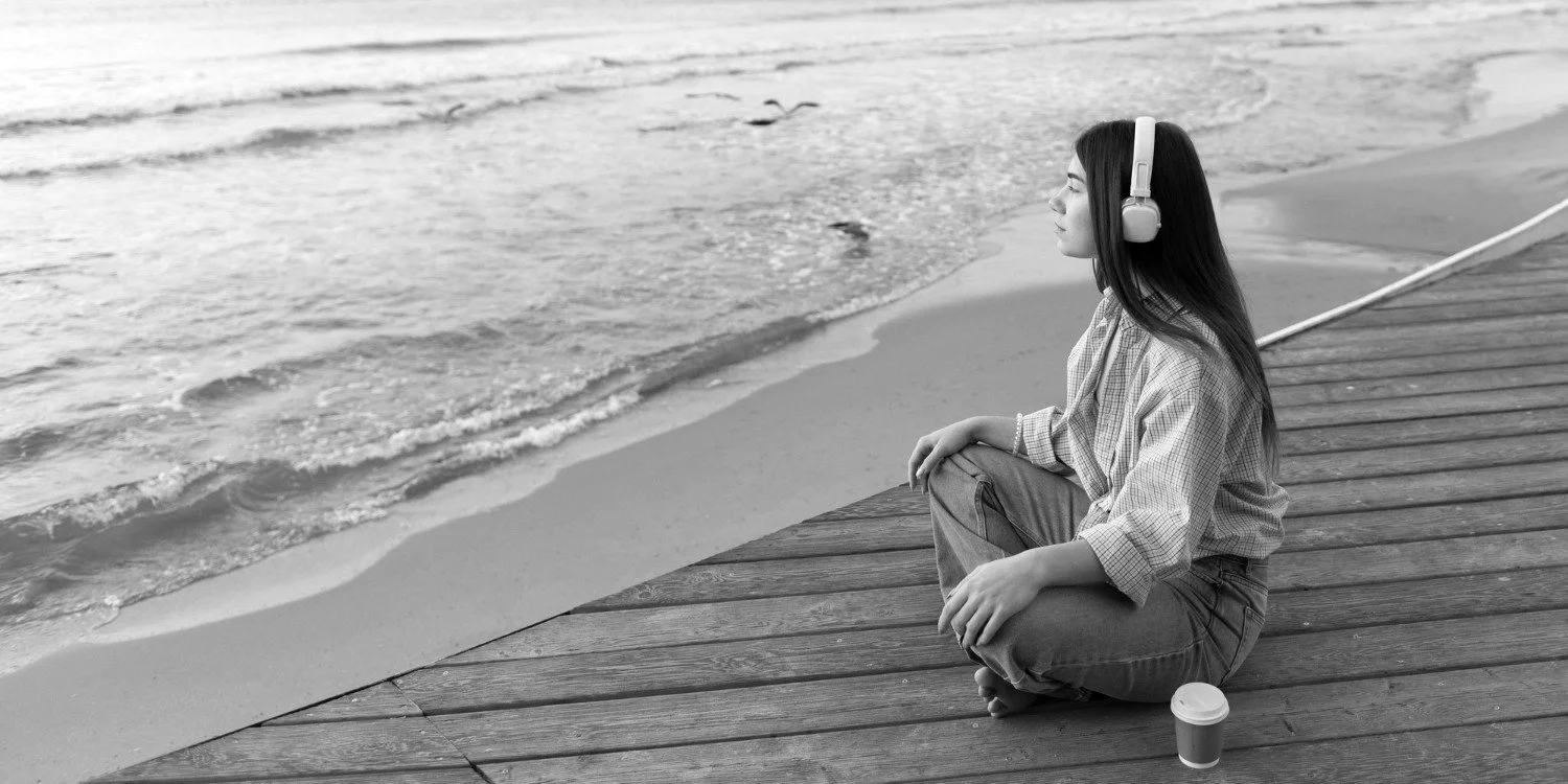 woman wearing headphones looking out onto a beach depicting someone who could be in burnout recovery
