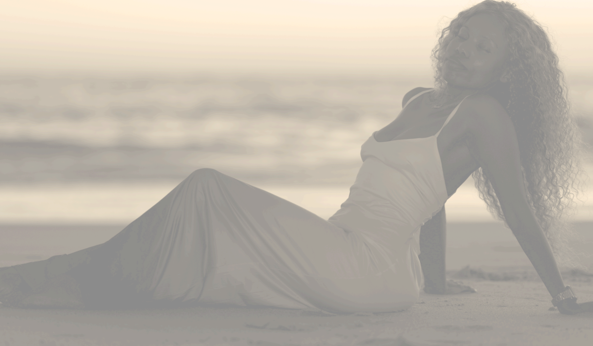 Woman relaxing on the beach during sunset, sitting on sand with the ocean in the background.