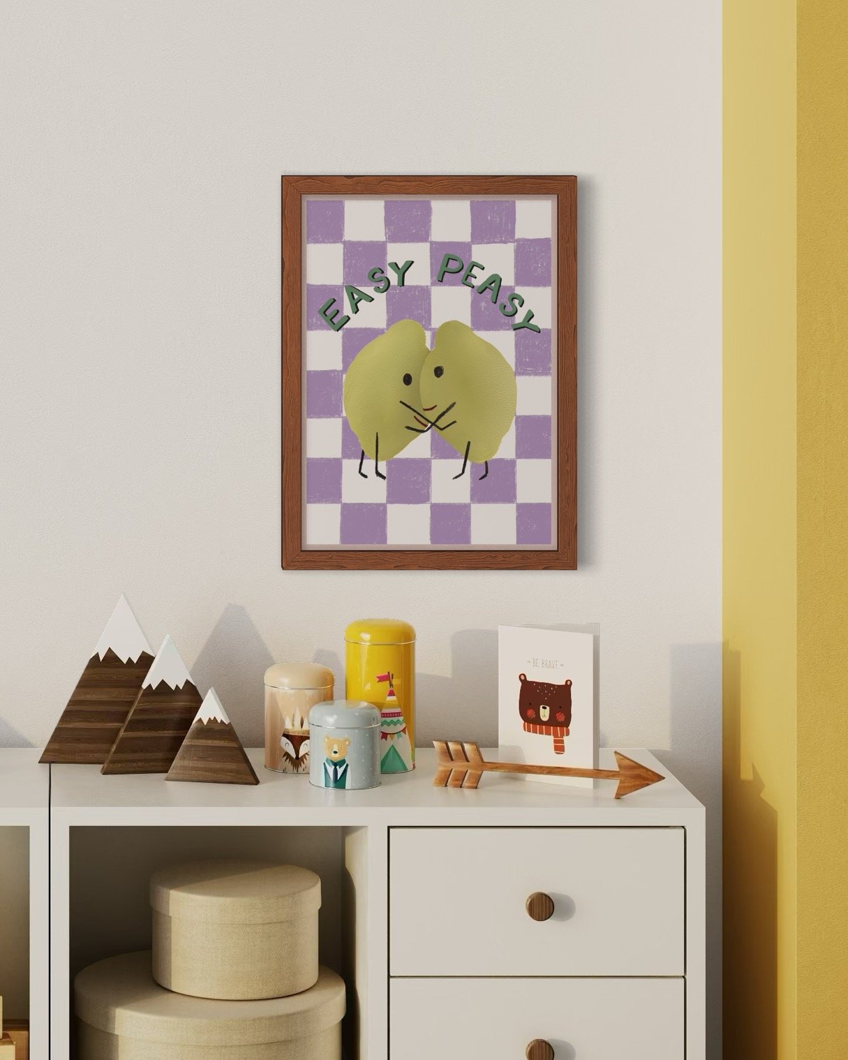Decorative wall art featuring a cute illustration of two lemons  with the words 'Easy Peasy' above, hanging above a white cabinet with wooden knobs, decorated with mountain-shaped wooden decor, colourful tins, a framed card, and a wooden arrow.