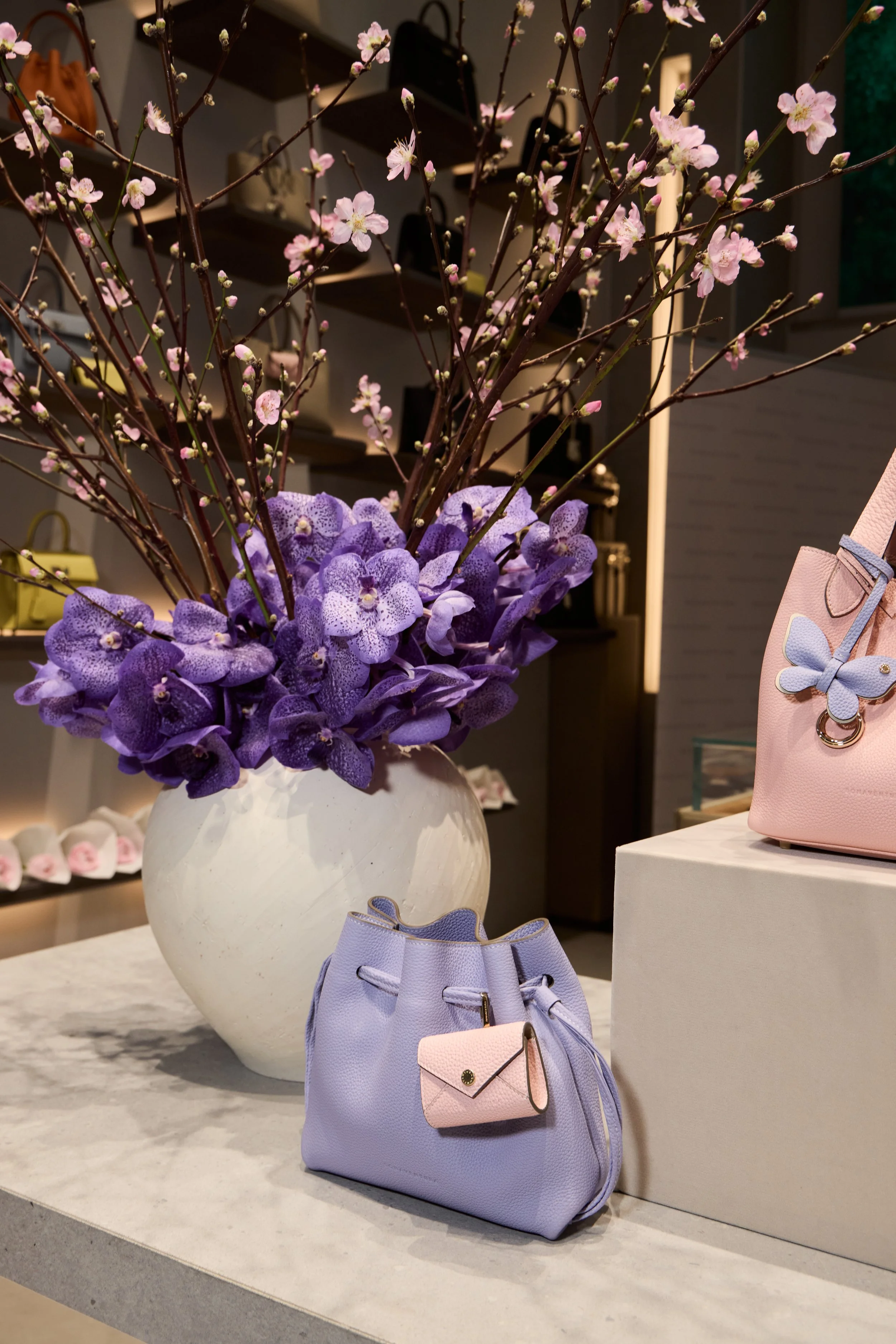 Vaso bianco con fiori di pesco rosa e orchidee viola, con borse e accessori da moda in studio di negozio