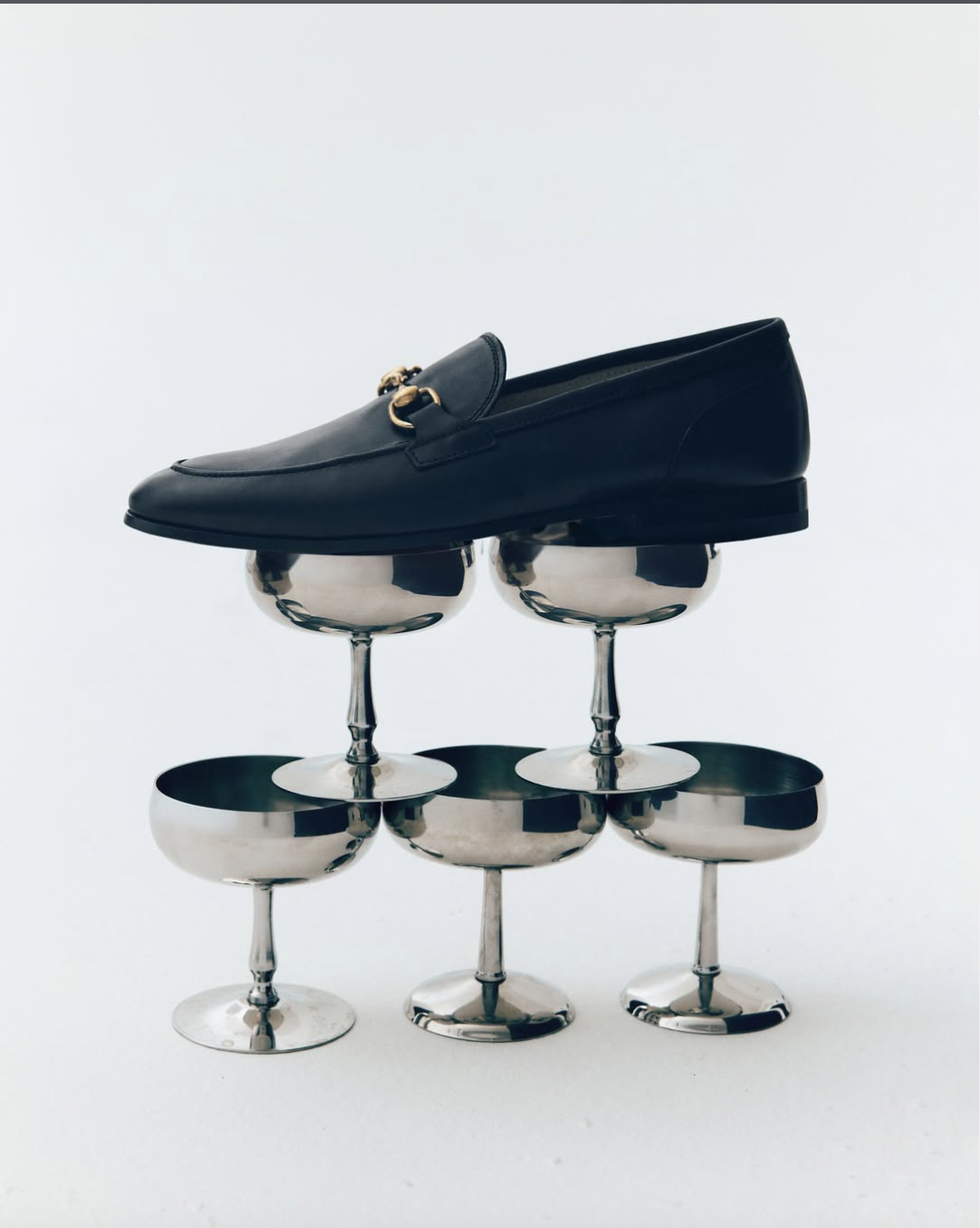 Una scarpa da uomo in pelle nera appoggiata su dei bicchieri di champagne rovesciati