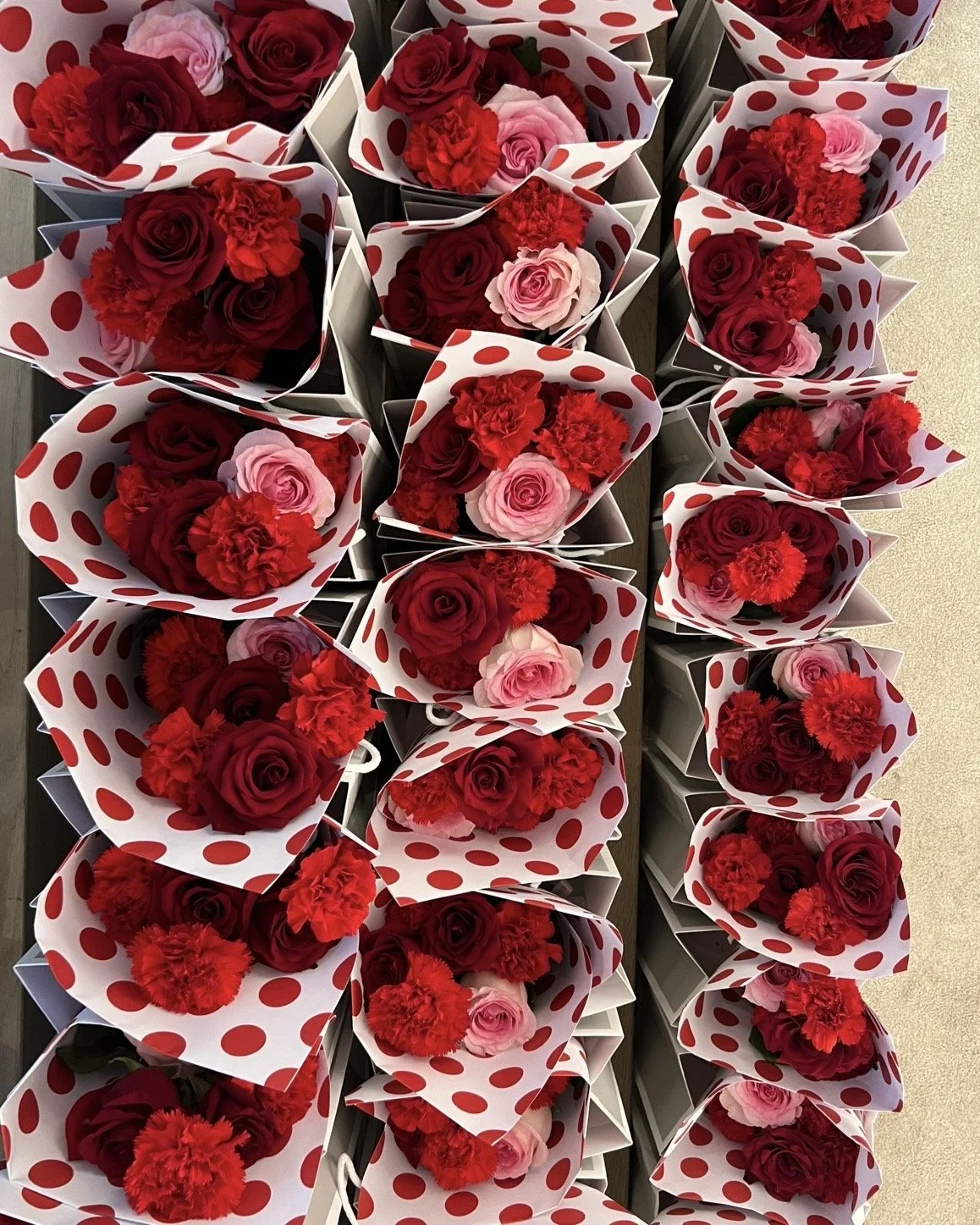Vasi di fiori rossi e rosa avvolti in carta con pois rossi su sfondo chiaro.