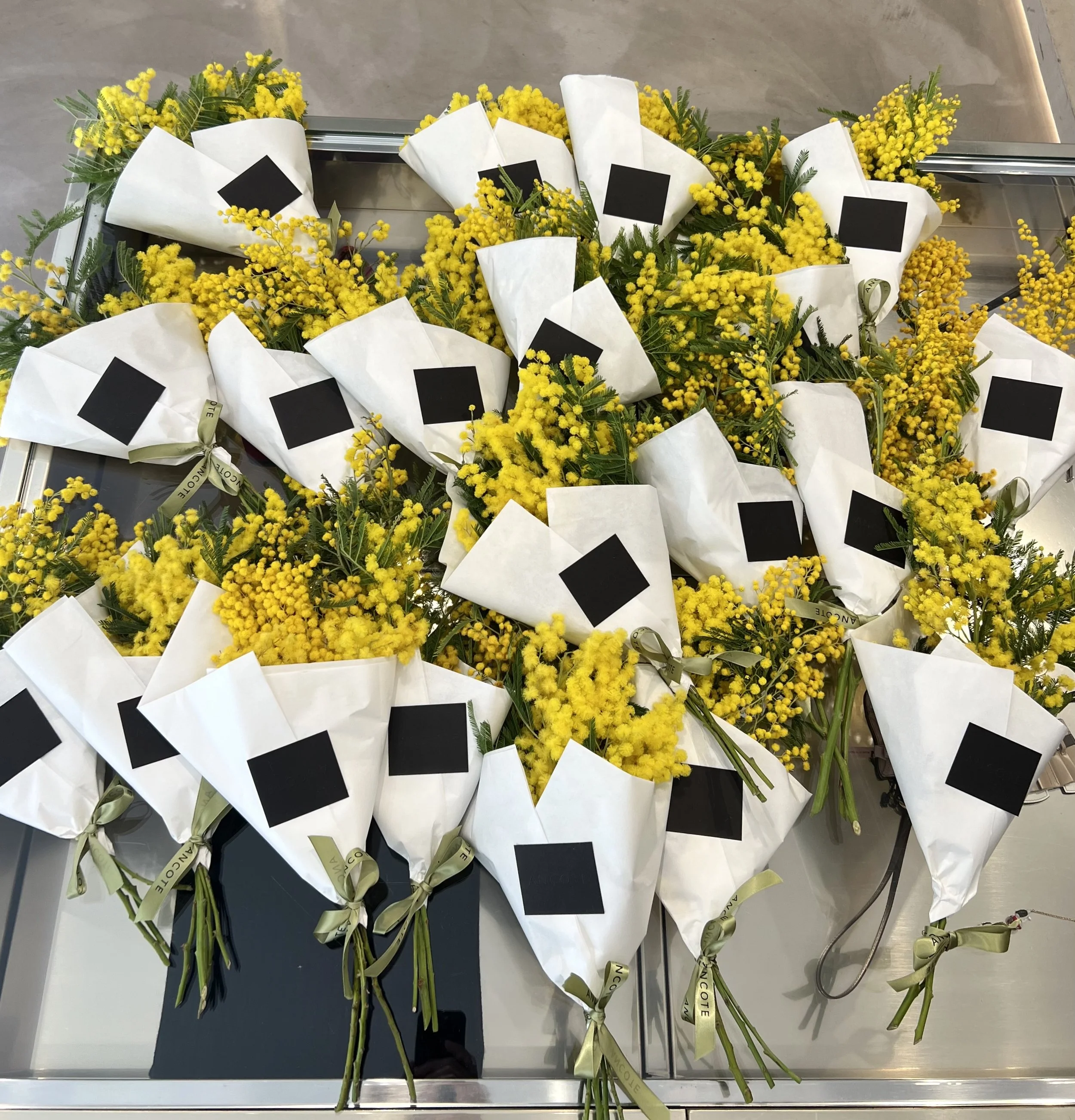 Mazzo di fiori gialli avvolti in carta bianca, legati con nastri raffinatamente annodati.