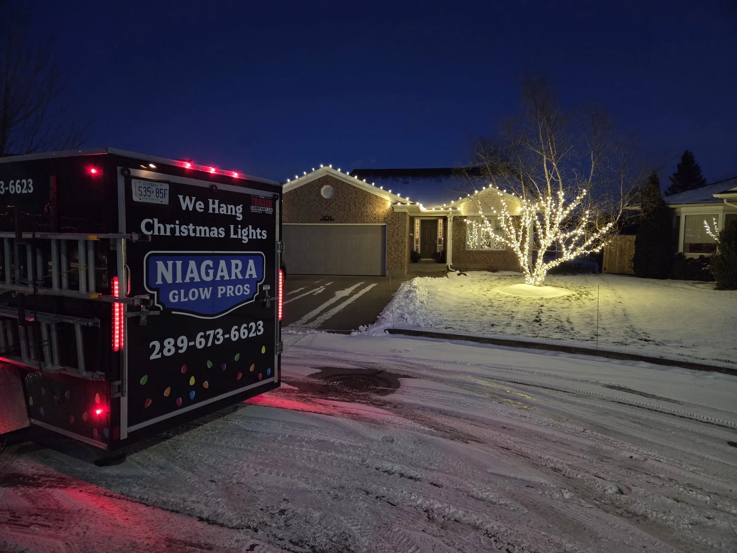 Snowy residential roofline and tree wrap with Niagara Glow Pros trailer in Niagara Falls.
