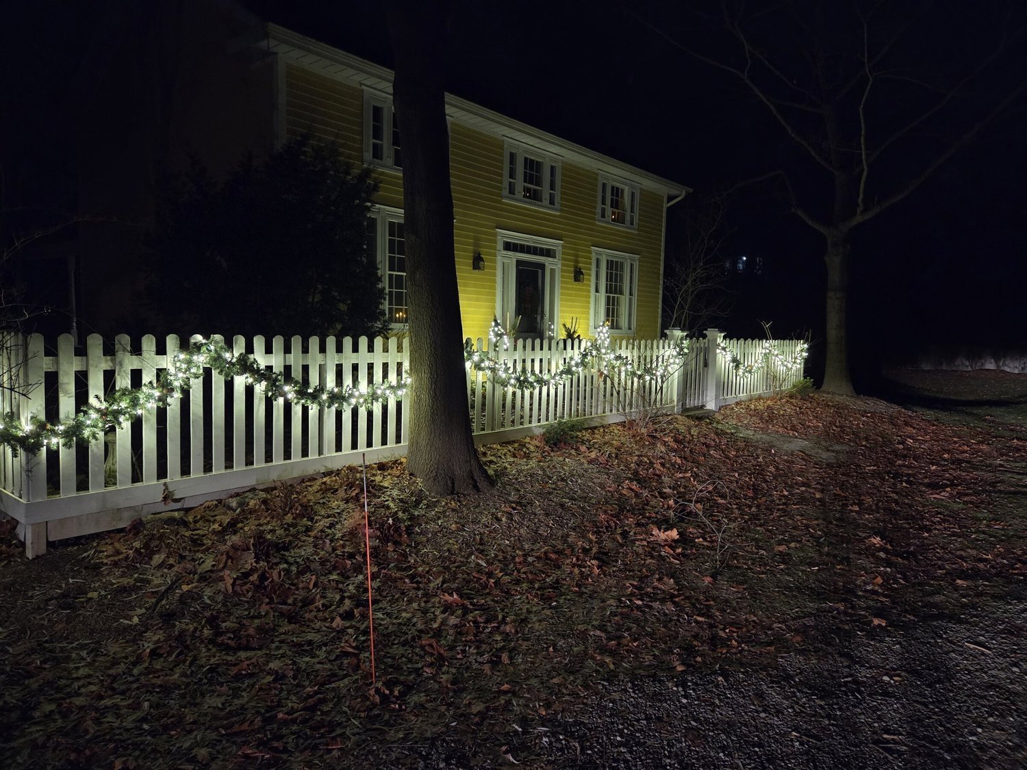 Lit evergreen fence garland on a white picket fence at a Niagara-on-the-Lake area home at night.