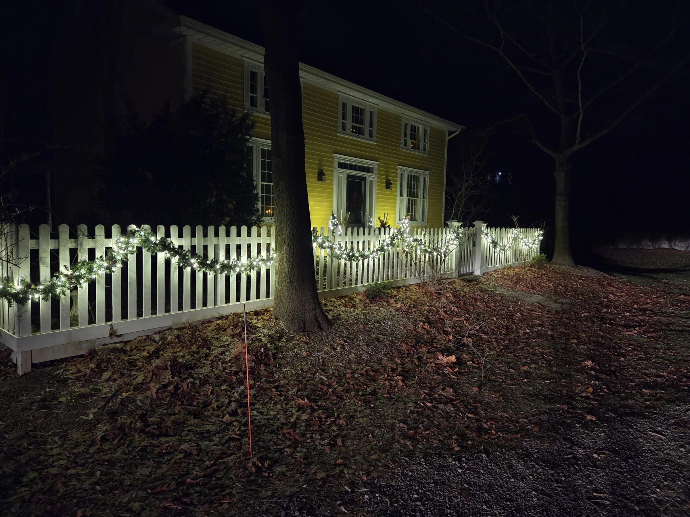 Lit evergreen fence garland on a white picket fence at a Niagara-on-the-Lake area home at night.