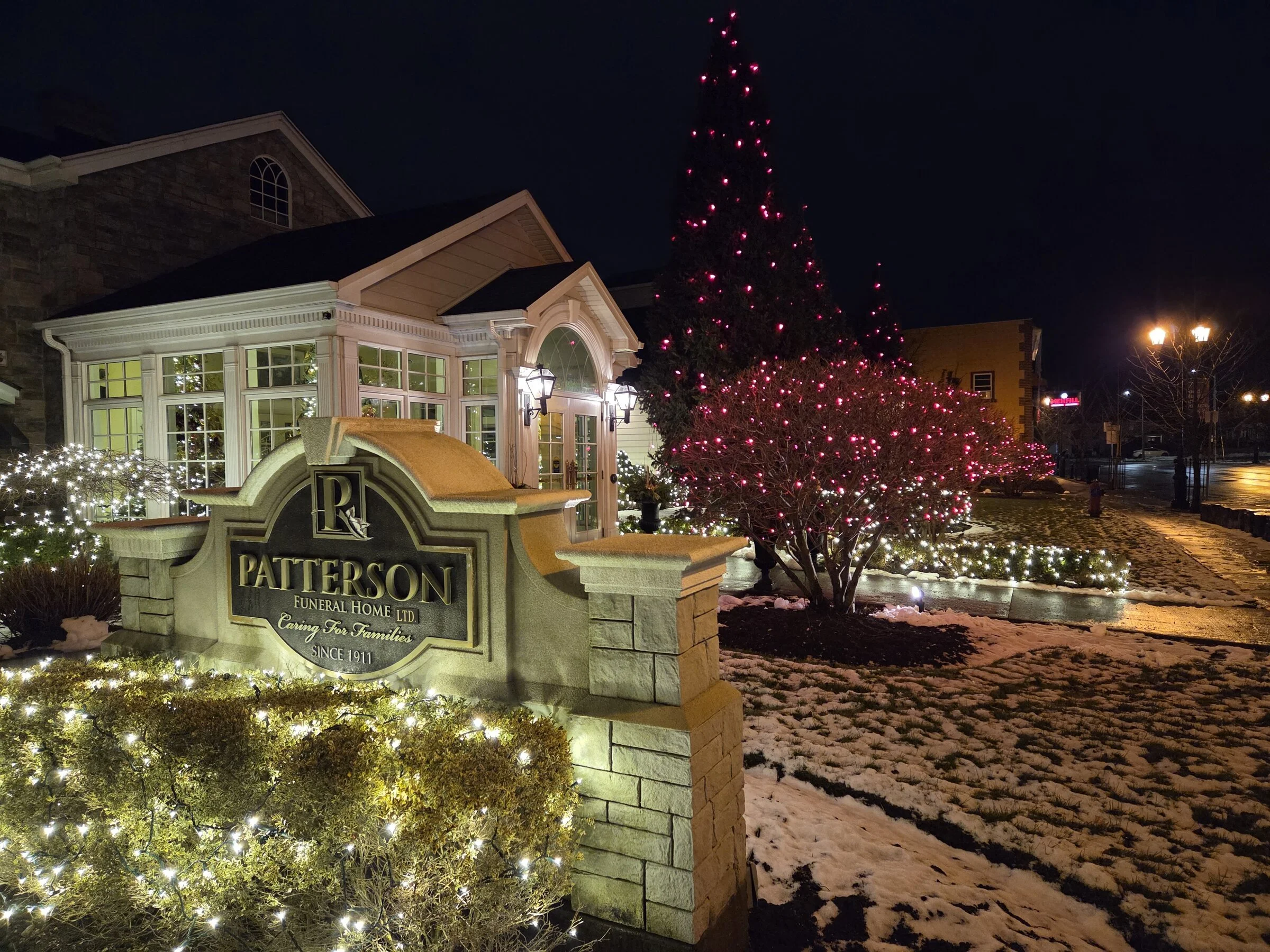 Commercial landscape with warm-white bush wraps and pink tree wrap at a Niagara Falls monument sign.