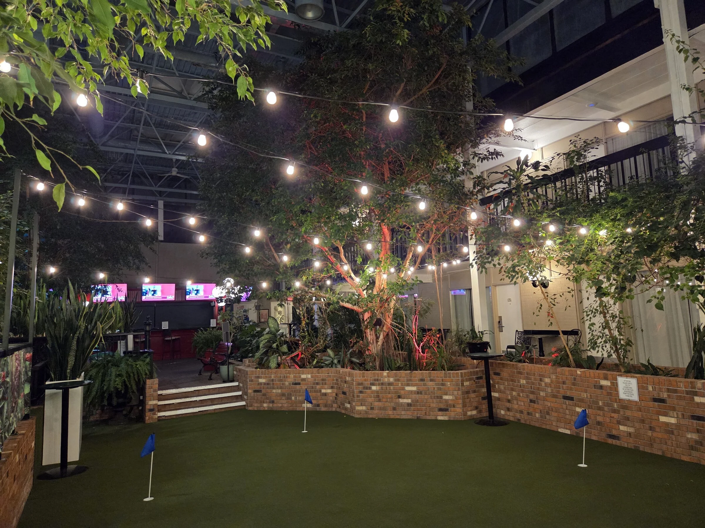 Wide hotel atrium hero shot with permanent bistro lights over turf, brick planters, trees, and lounge area in Niagara Falls.