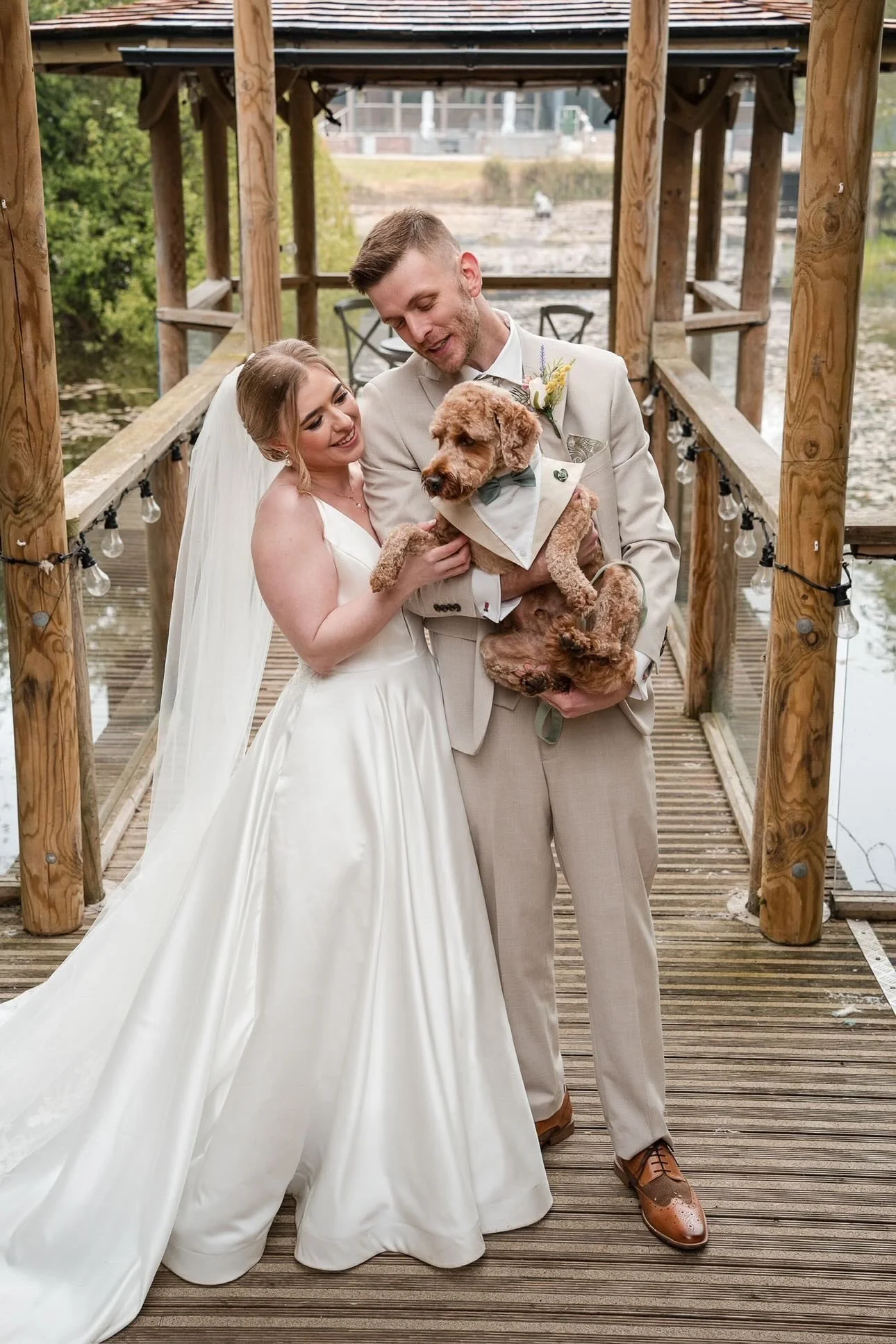 Bride and groom cuddling dog dressed in wedding day outfit 
