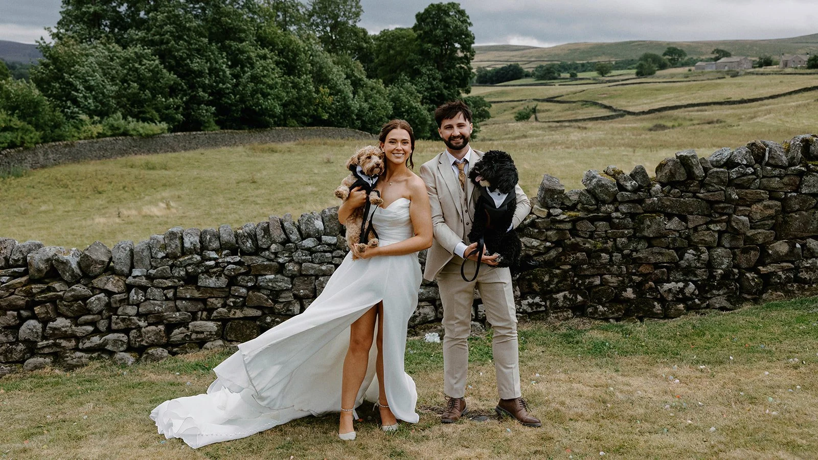 Bride and Groom stood holding a tan and black dogs with bow ties on