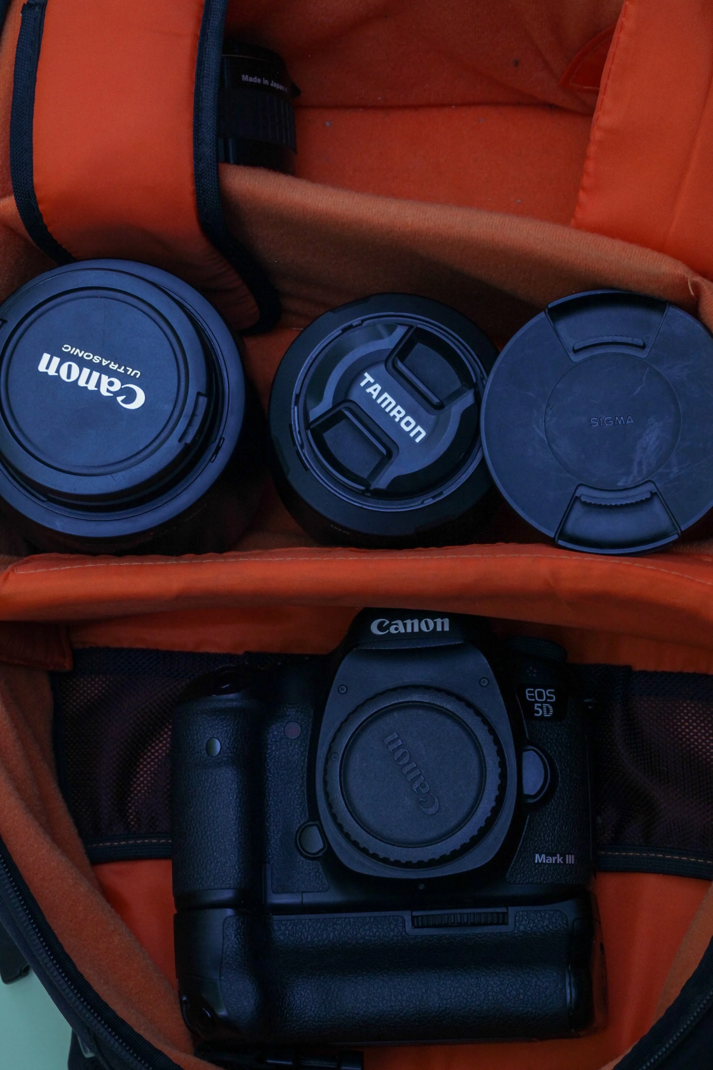 Un sac orange contenant un appareil photo Canon EOS 5D Mark III et trois objectifs avec leurs capuchons