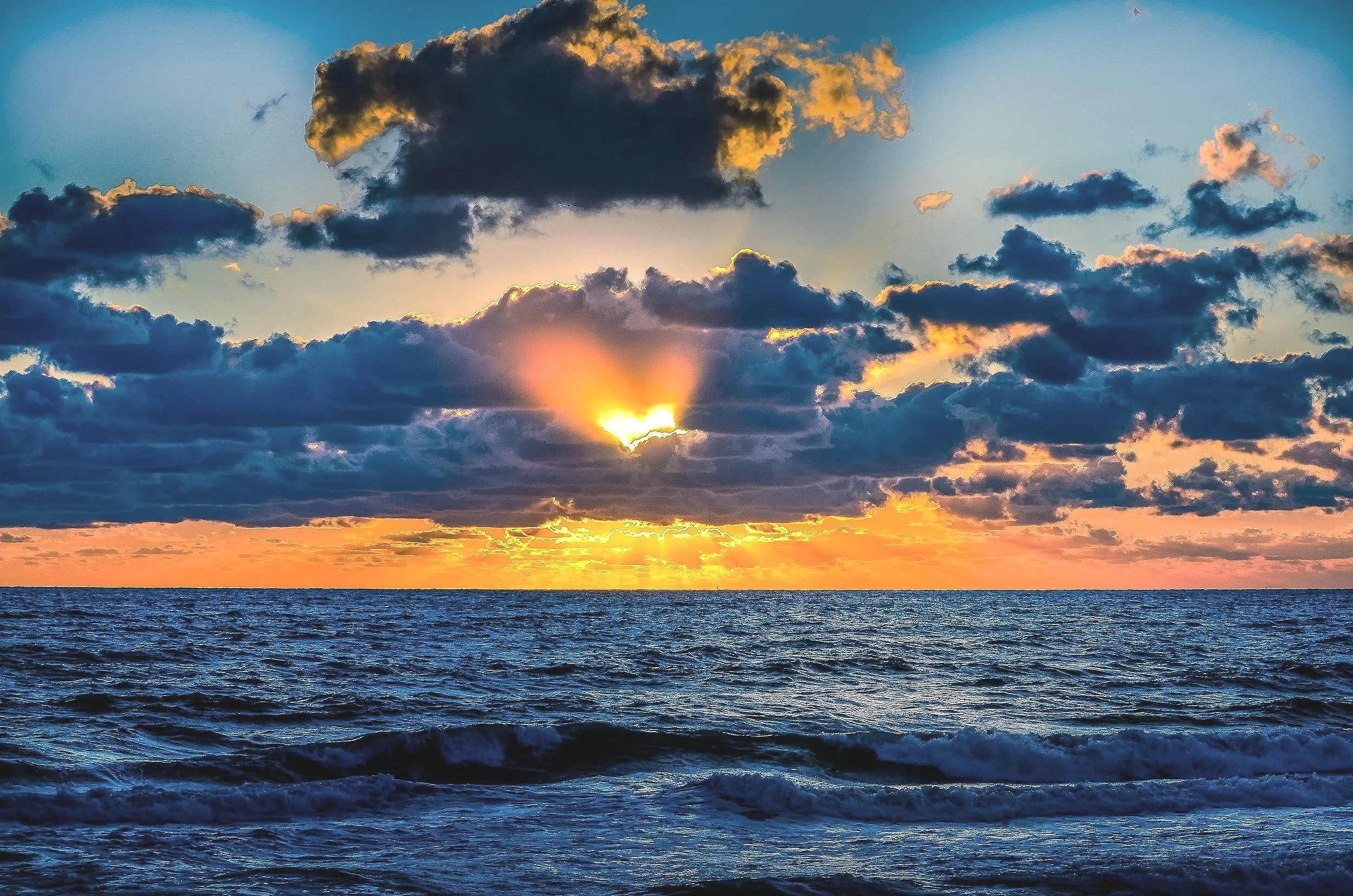 Sunset over the ocean with dark clouds and orange sky, waves crashing on the shoreline.