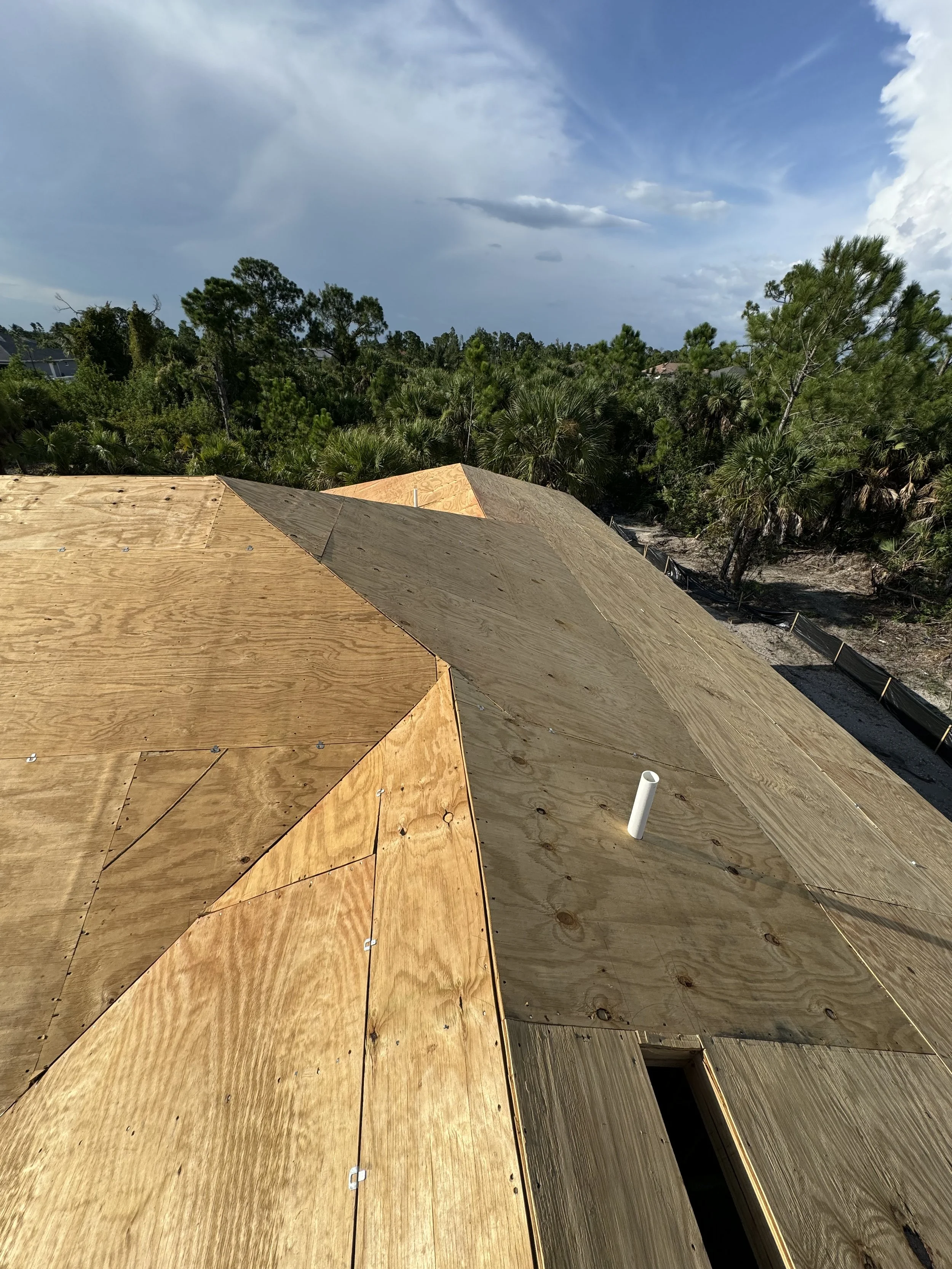 Construction site with a wooden roof under construction, overlooking a lush green landscape with trees and a cloudy sky.