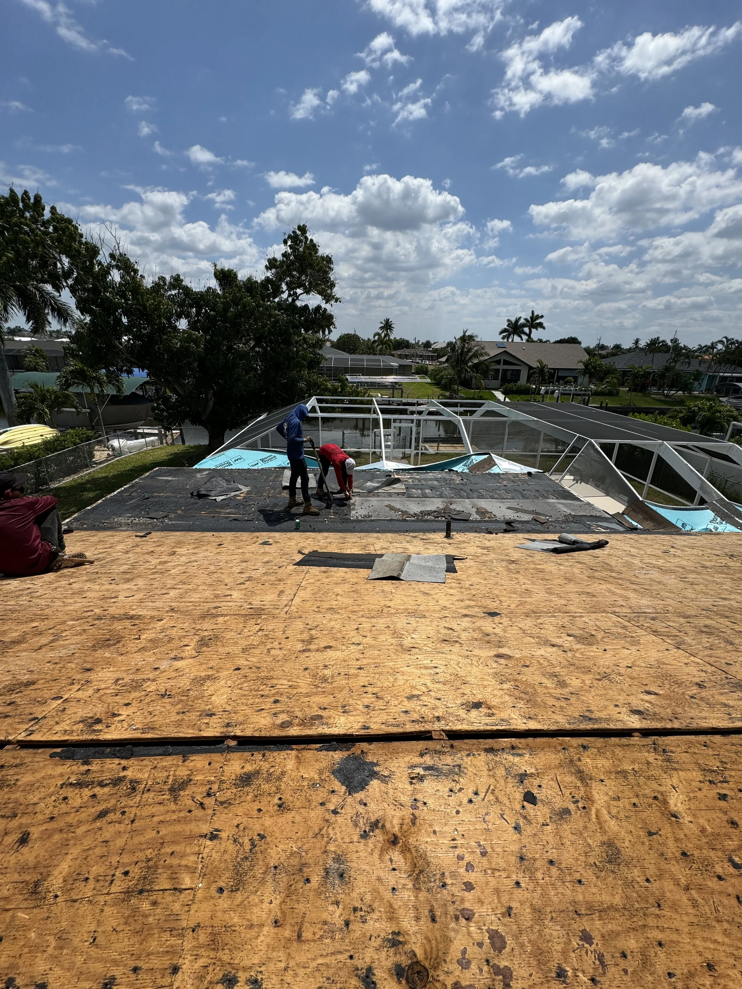 People working on a roof renovation under a partly cloudy sky in a residential neighborhood.