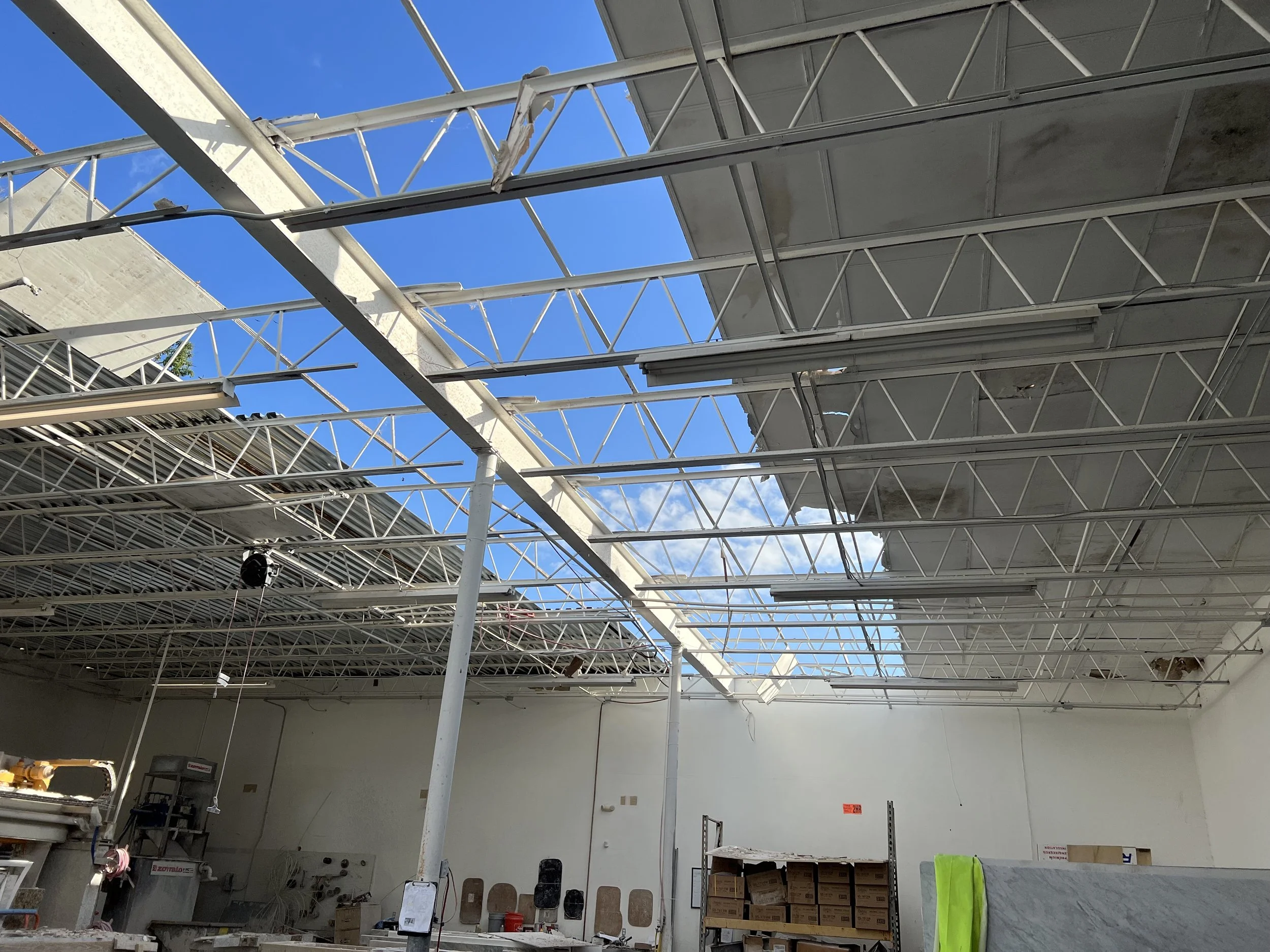 Construction site with a partially completed ceiling framework and scaffolding, with blue sky visible through open sections.