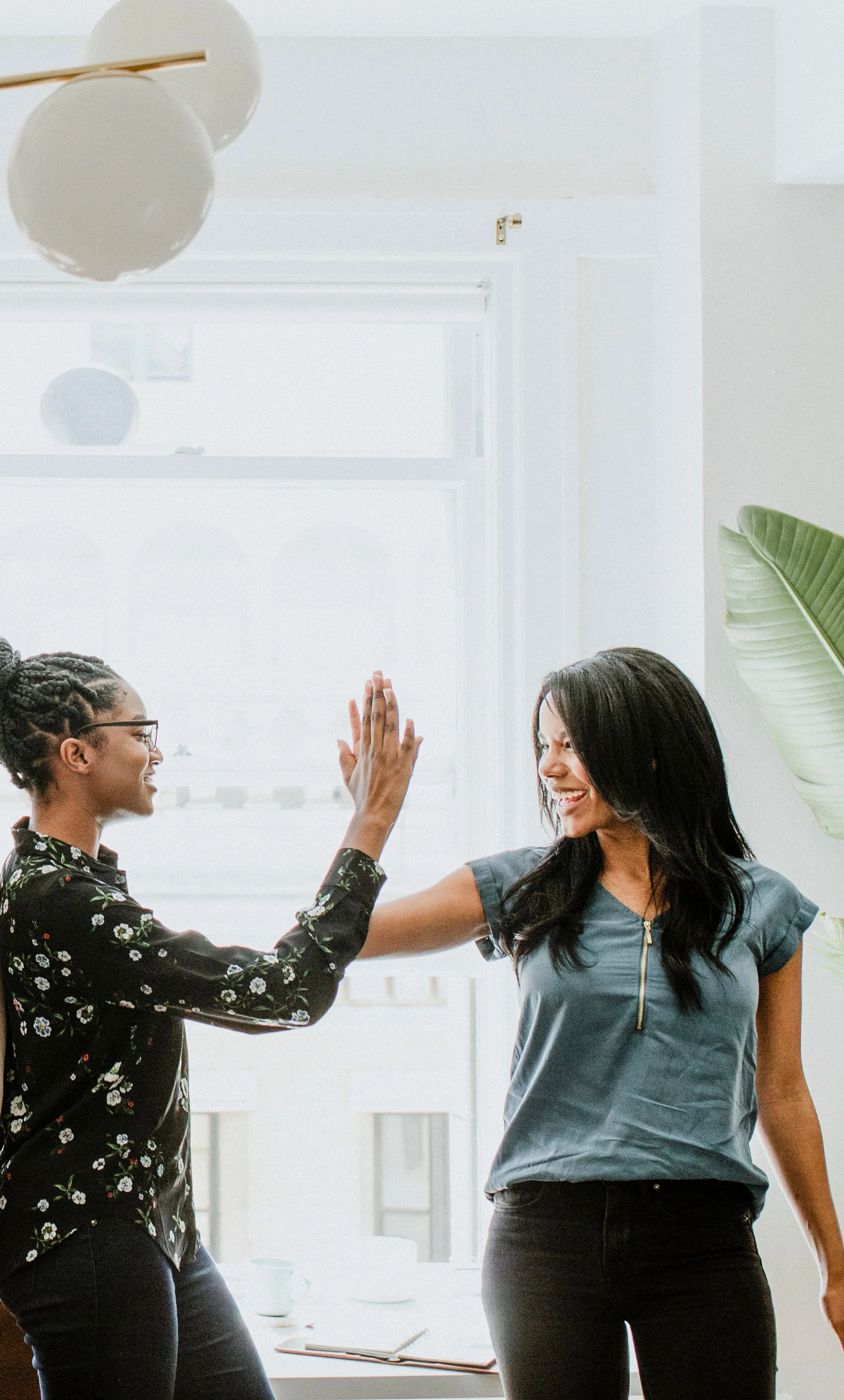 Two mothers sharing a high five, representing the community built in Motherwell's Postpartum Circle in Austin and Cedar Park, TX