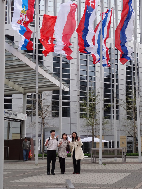 Three people standing in front of a modern office building with European flags flying overhead.