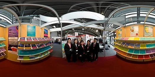 Group of five women in business attire standing in an exhibition hall with shelves of colorful materials.
