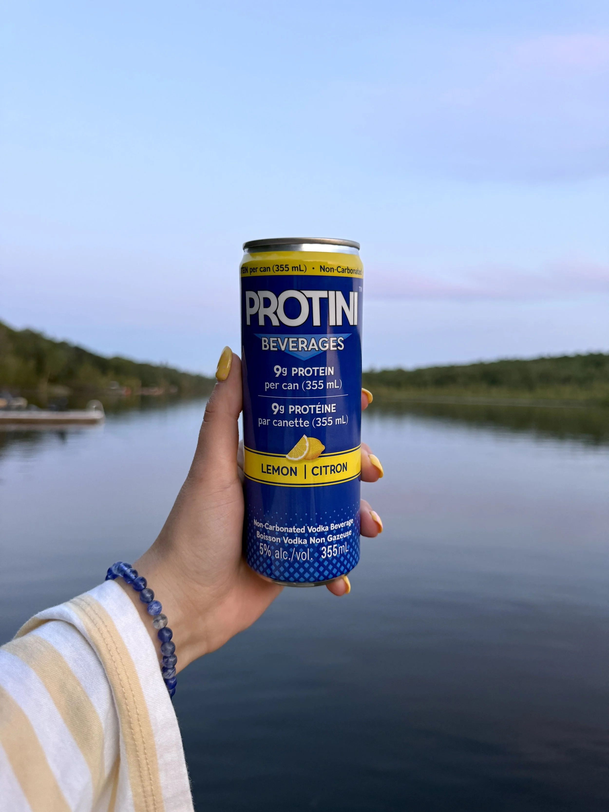 Cans of Protini vodka beverage with lemon flavour, stacked on a store shelf, featuring blue and yellow packaging.