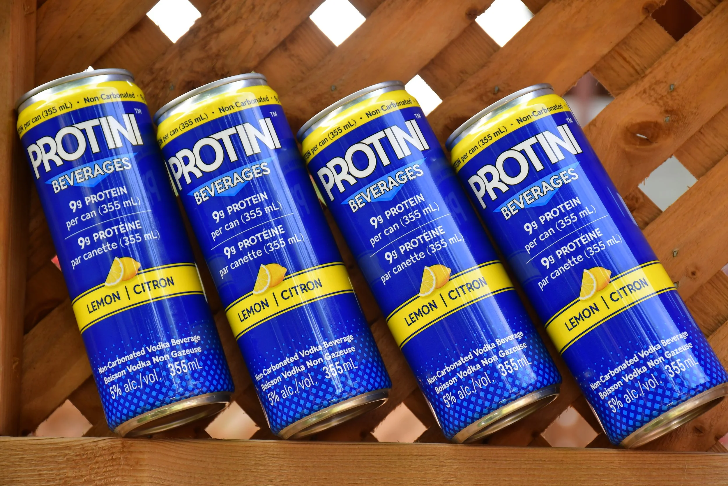 Cans of Protini lemon-flavored vodka beverage surrounded by fresh yellow lemons on a bed of ice.